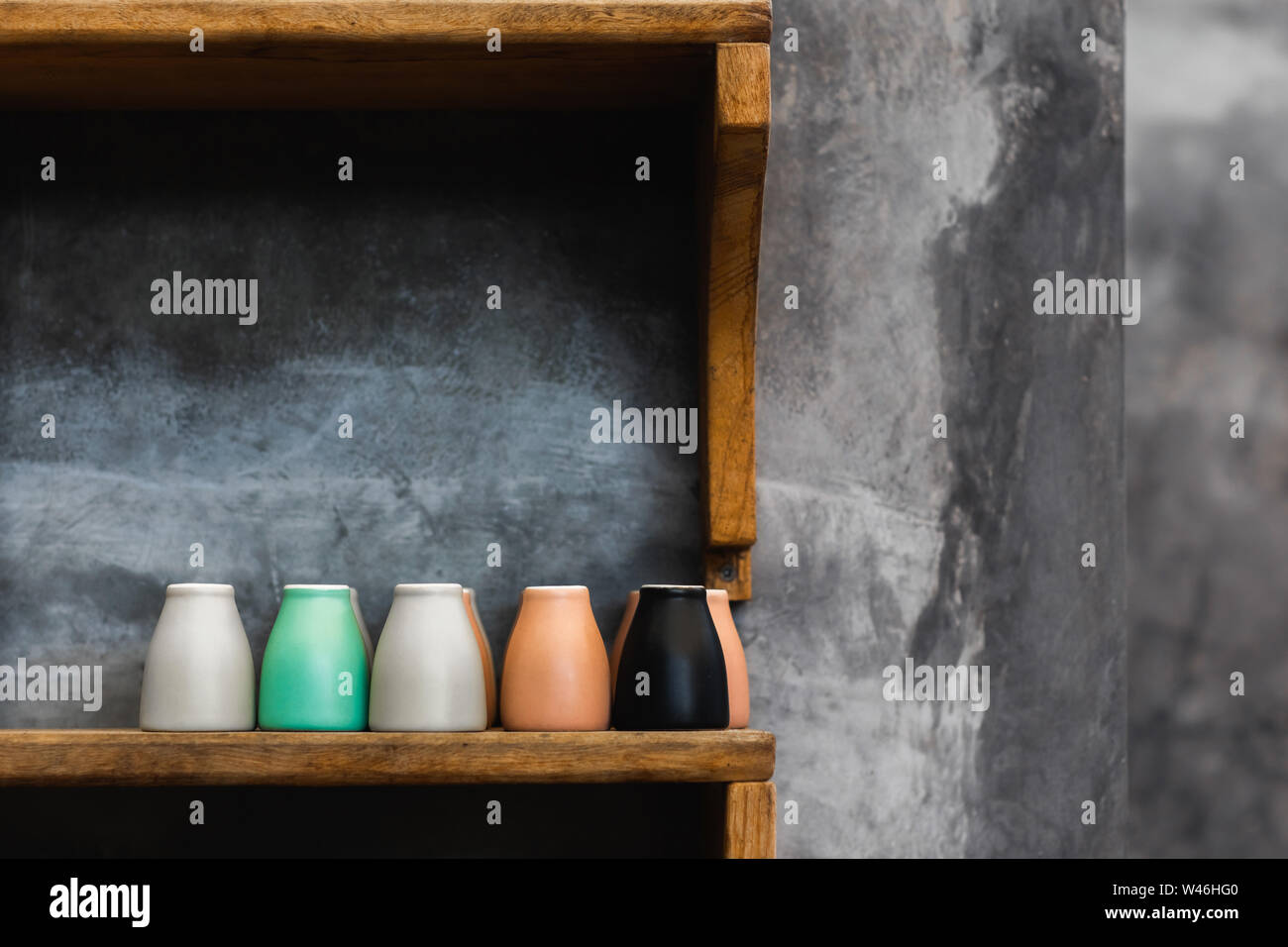 Different colorful coffee cups on wooden shelf in cafe. Background of gray concrete cement wall. Trendy interior design, hipster cafe. Empty space for Stock Photo