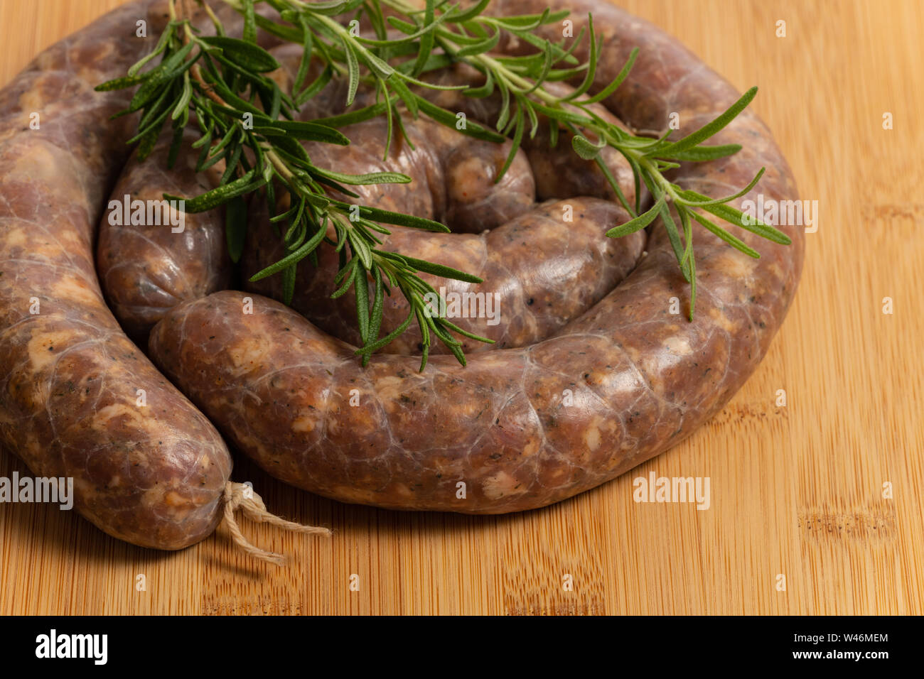 Raw homemade stuffed pork sausages and rosmarin isolated on a wood board. Stock Photo