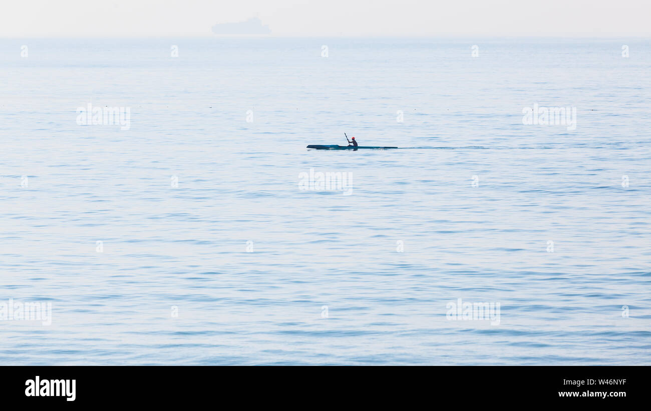 Surf ski canoe paddler on ocean waters silhouetted horizon landscape. Stock Photo