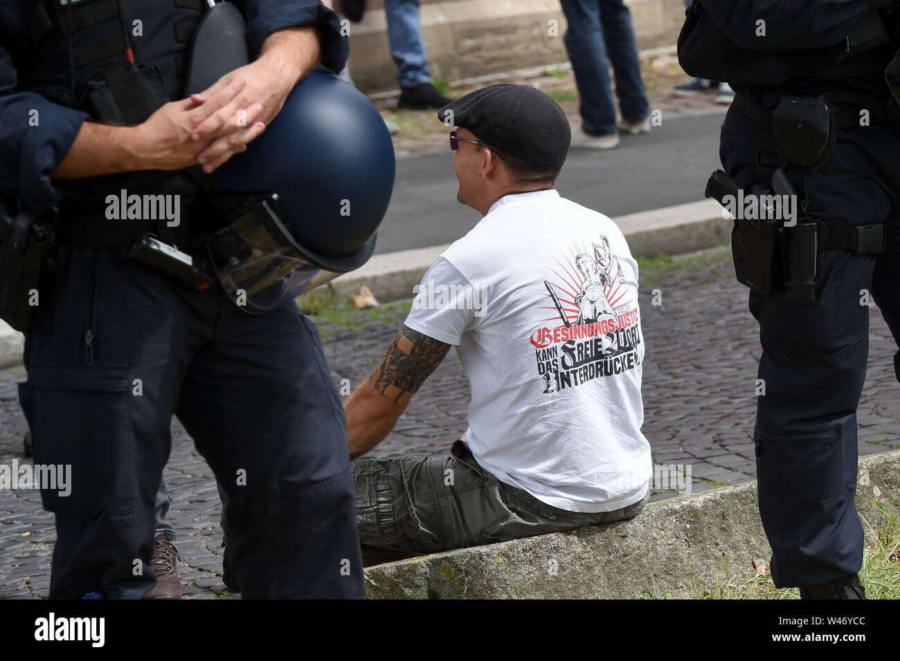 Hanover, Germany. Kassel, Germany. 20th July, 2019. A supporter of the small right-wing extremist party 'Die Rechte' sits behind two police officers in front of the demonstration. The party had called for a demonstration in Kassel against media prejudgement in connection with the Lübcke case. A massive police presence is to prevent possible riots between the two camps. Credit: Uwe Zucchi/dpa/Alamy Live News Stock Photo