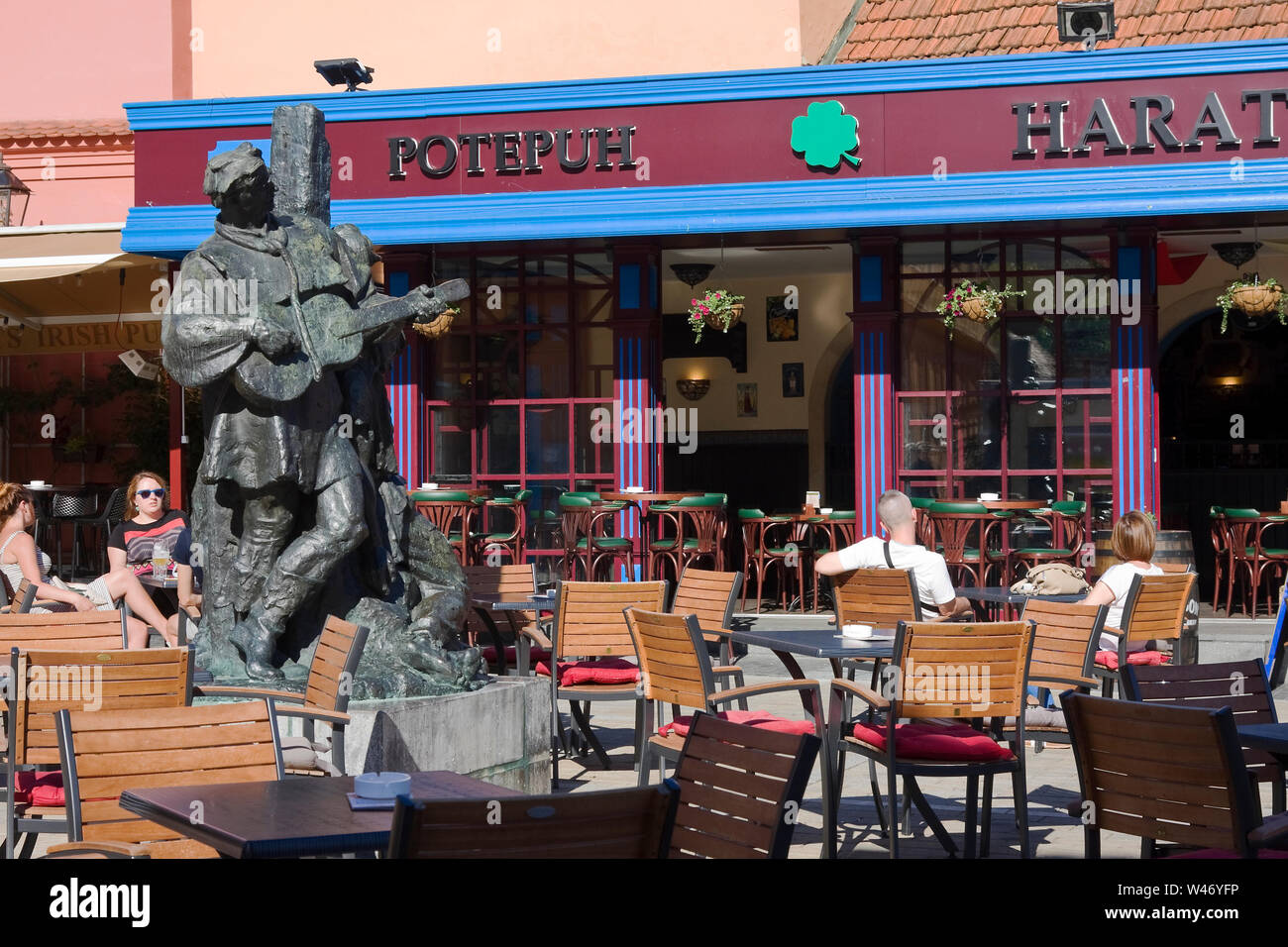 outdoor tables; people drinking, eating, Petrica Kerempuh bronze statue, 1955, Croatian jester, relaxation, Irish Pub; Zagreb; Croatia; Europe; summer Stock Photo