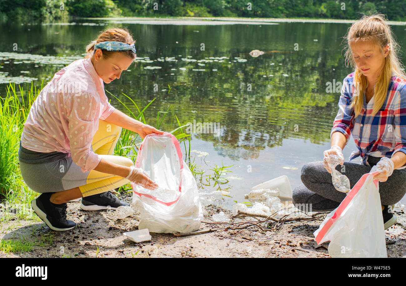 Volunteers cleaning garbage near river. Women picking up a bottle plastic in the lake, pollution