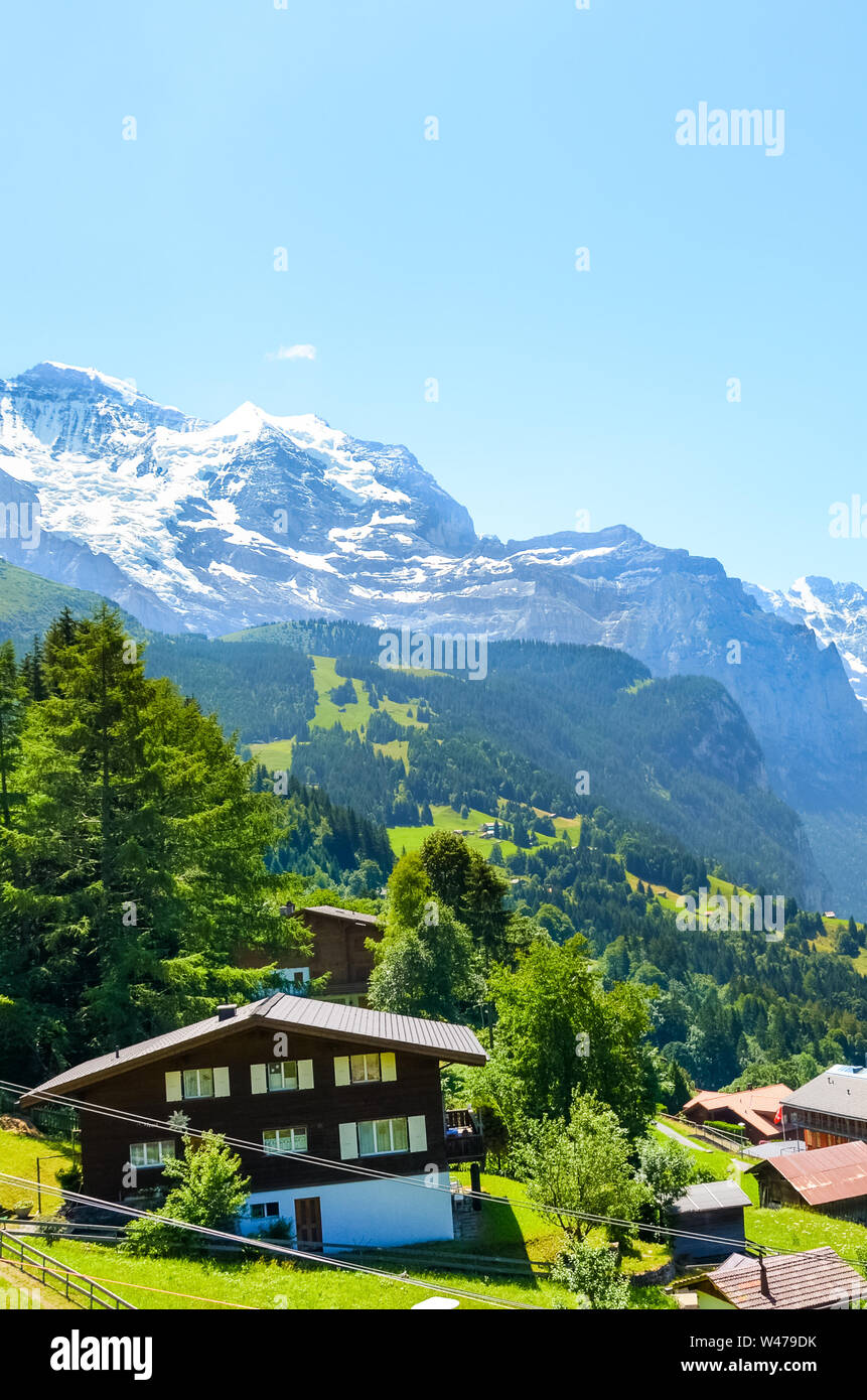 Stunning village Wengen in Swiss Alps. Mountain ridges with snow on top in background. Switzerland summer. Alpine landscape. Mountain chalets. Popular resort. Tourist place. Stock Photo