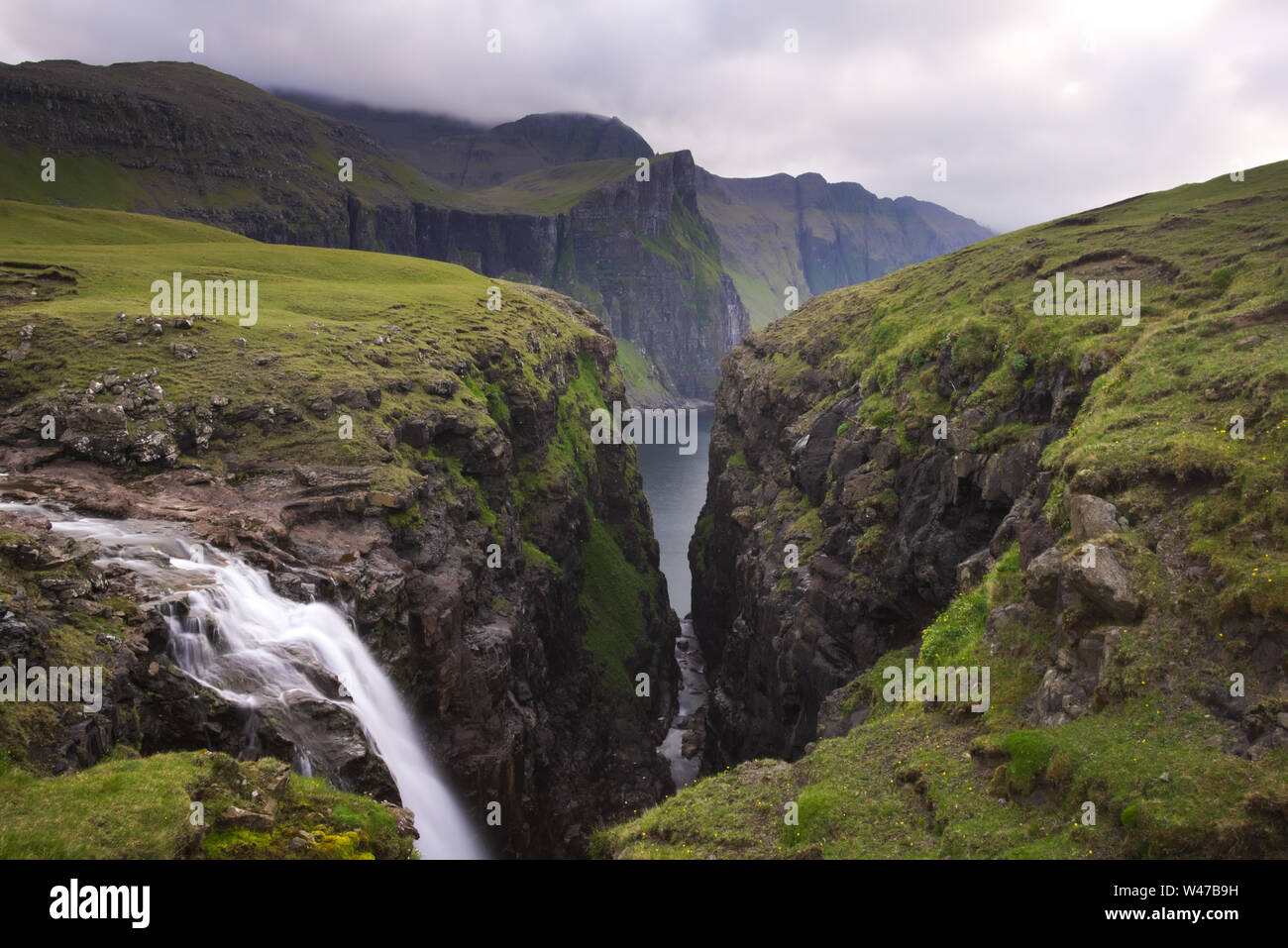 Waterfall and sea cliffs at the end of Fjallavatn, island of Vágar, the Faroe islands, in summer Stock Photo