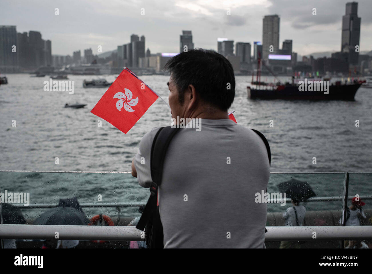A man holding Hong Kong flags observes boats with messages at Victoria Harbour while participating of pro-government Safeguard Hong Kong rally at Tamar Park.Government supporters show up in number of tens of thousands in a pro-police rally, at Tamar Park.  Named Safeguard Hong Kong,  the demonstration was co-organized by 70 pro-Beijing figures and  was attended by local residents, mainland immigrants, members of ethnic minorities, as well as visitors from across the border. Stock Photo