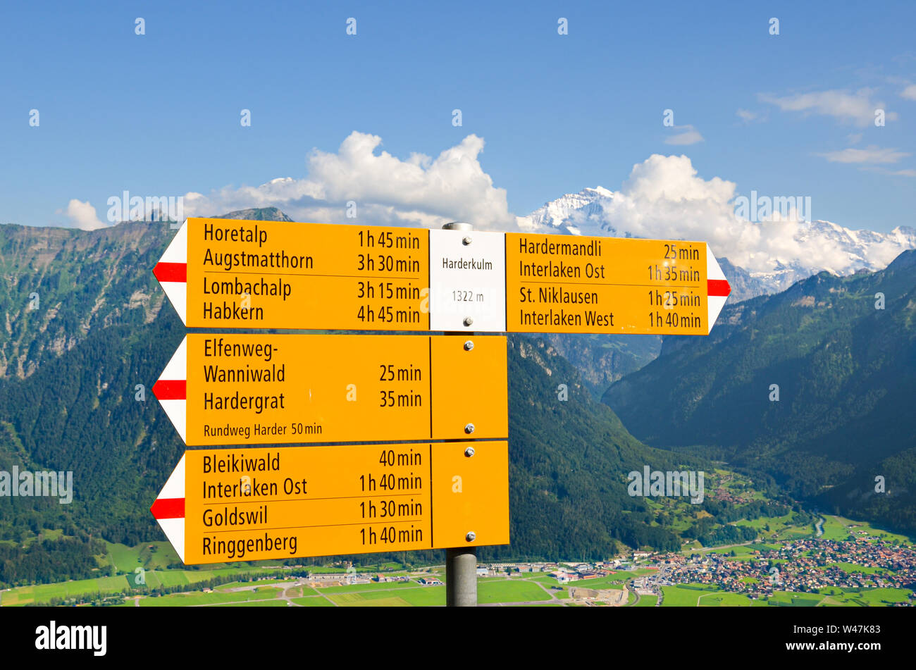 Yellow tourist sign on the top of Harder Kulm, Interlaken, Switzerland. The information sign specifies the directions and distances. Amazing summer Alpine landscape in background. Swiss Alps, tourism. Stock Photo
