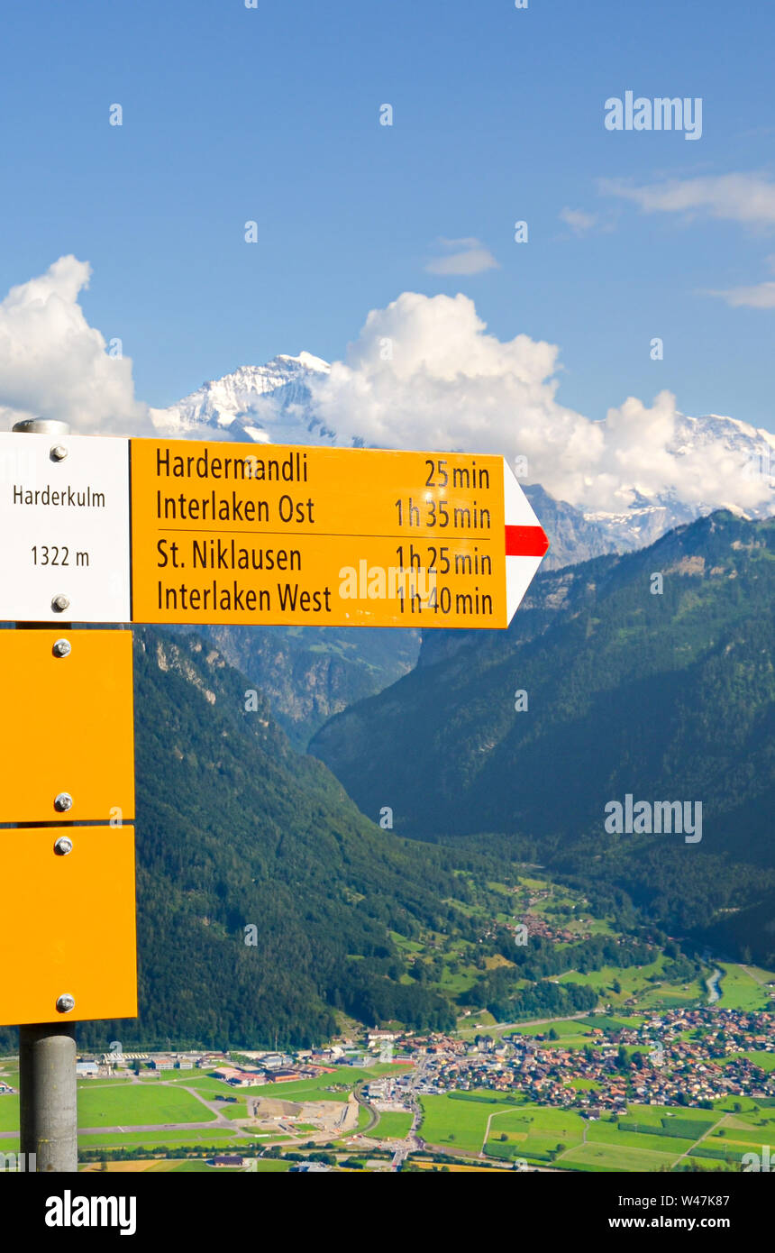 Yellow information sign on top of Harder Kulm, Interlaken, Switzerland. The tourist sign specifies the distances and directions. Beautiful summer Alpine landscape in background. Swiss Alps, tourism. Stock Photo