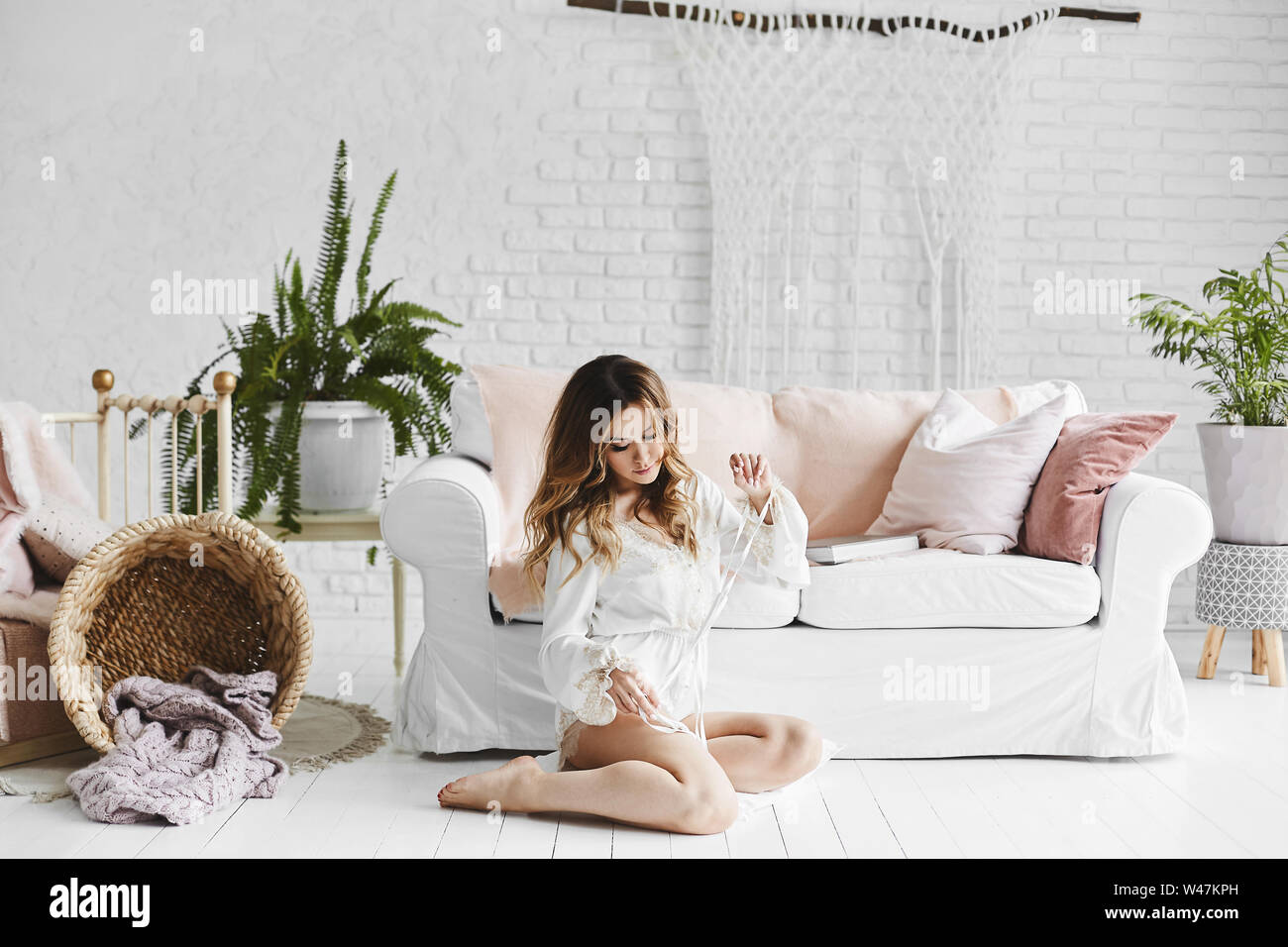 Young woman in white dress sitting on floor in living room Stock Photo