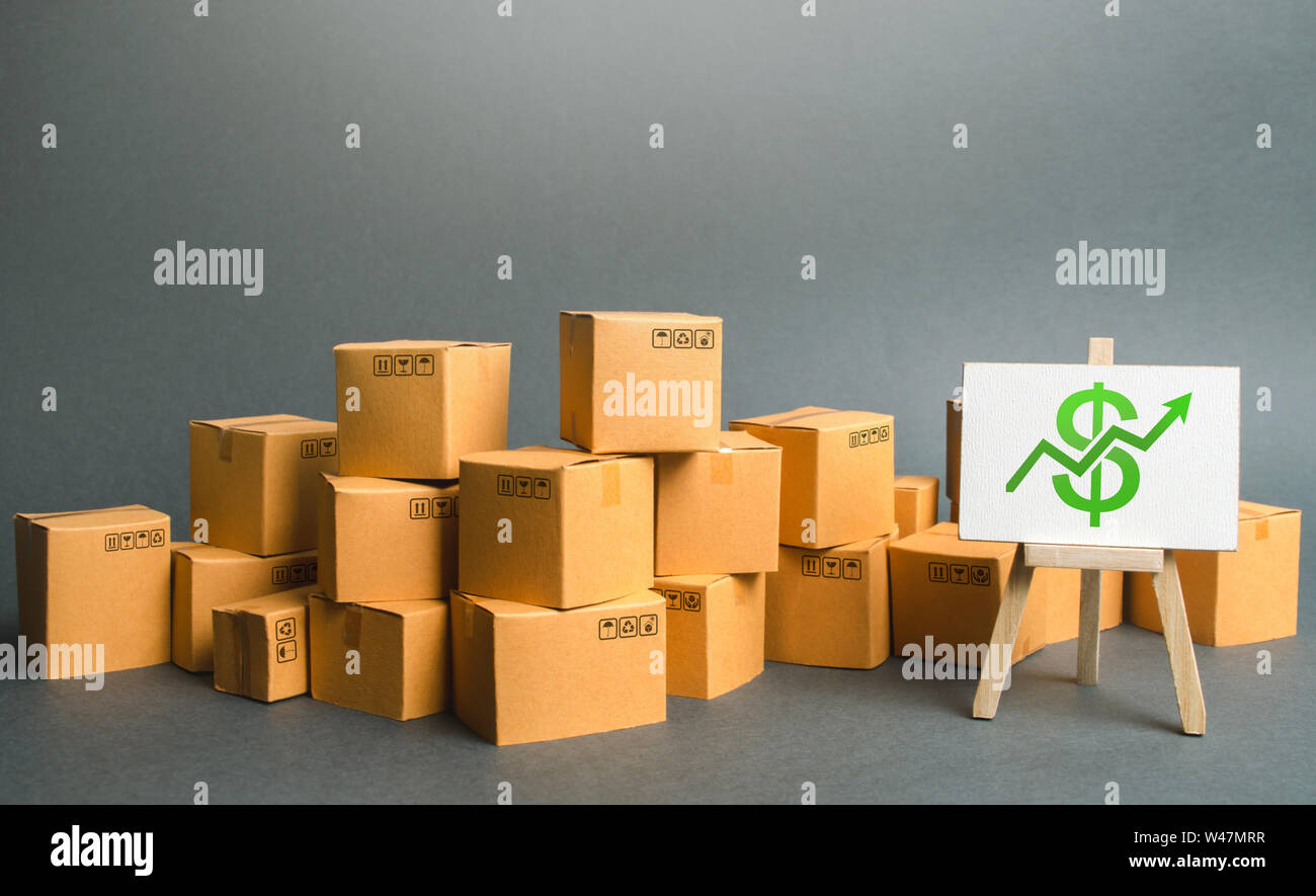 Plenty of cardboard boxes and sign with a dollar symbol green up arrow. rate growth of production of goods and products, increasing economic indicator Stock Photo