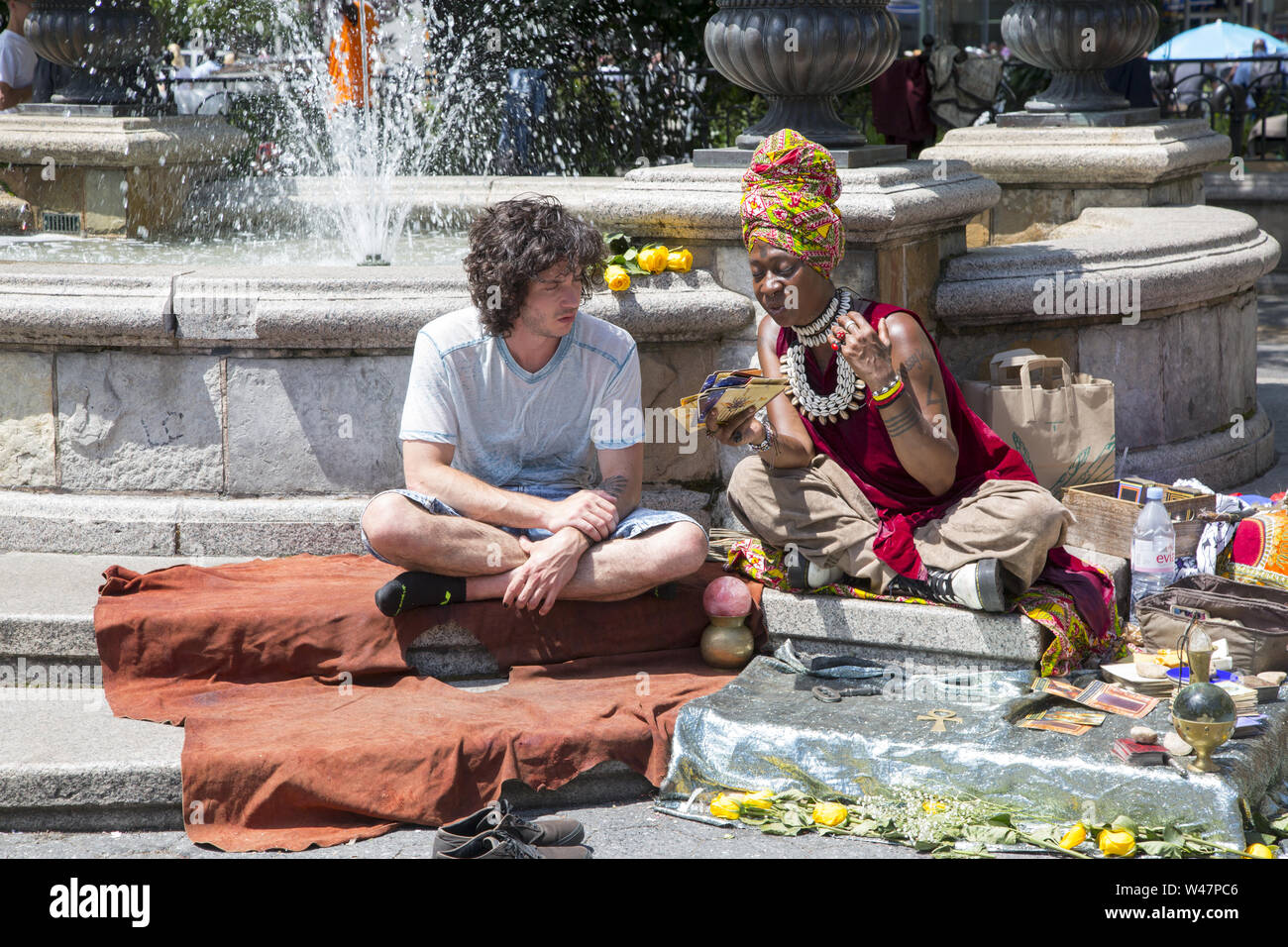 Young man consults a card reading fortune teller near the fountain in Union Square where she advises people about their possible futures. Manhattan, New York City. Stock Photo