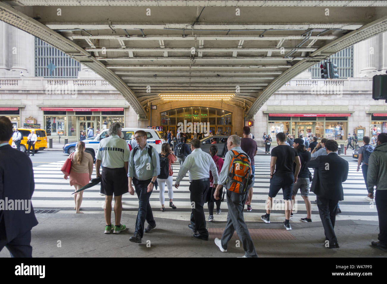 People cross 42nd Street into and out from Grand Central Terminal at Pershing Square with the Park Avenue Bridge above. Stock Photo