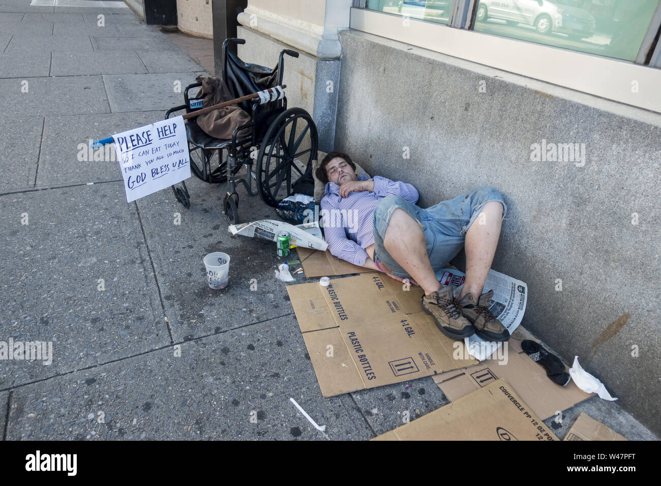 Disabled homeless man sleeps along the sidewalk on Kings Highway in the morning in the Midwood