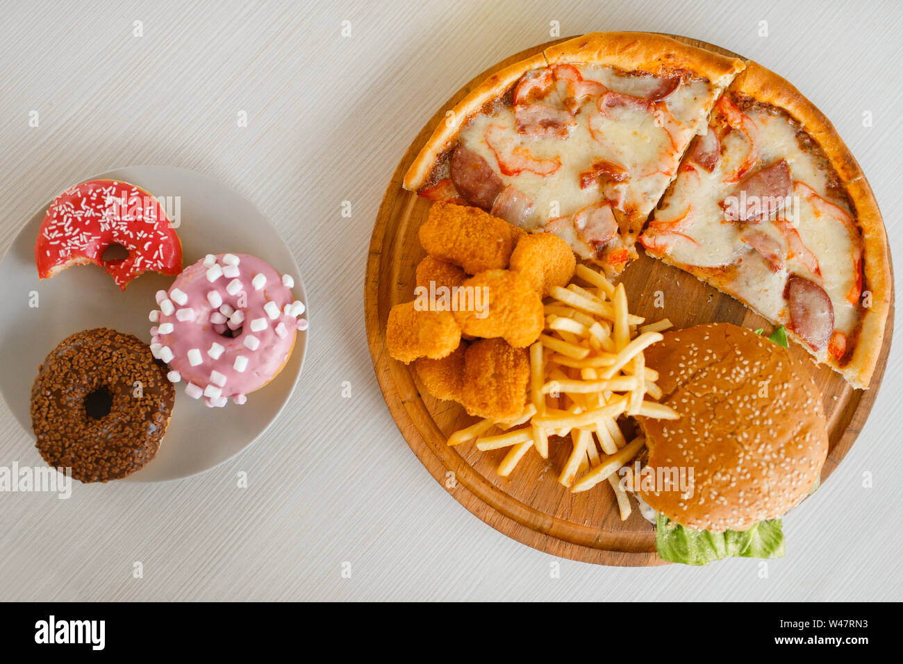 High calorie food on the table, top view, nobody. Pizza and burger, doughnuts, french fries and chicken nuggets. Junk fastfood Stock Photo