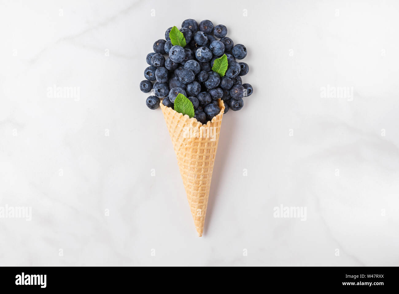blueberries with mint in waffle ice cream cone on white marble background. summer food concept. top view. flat lay Stock Photo