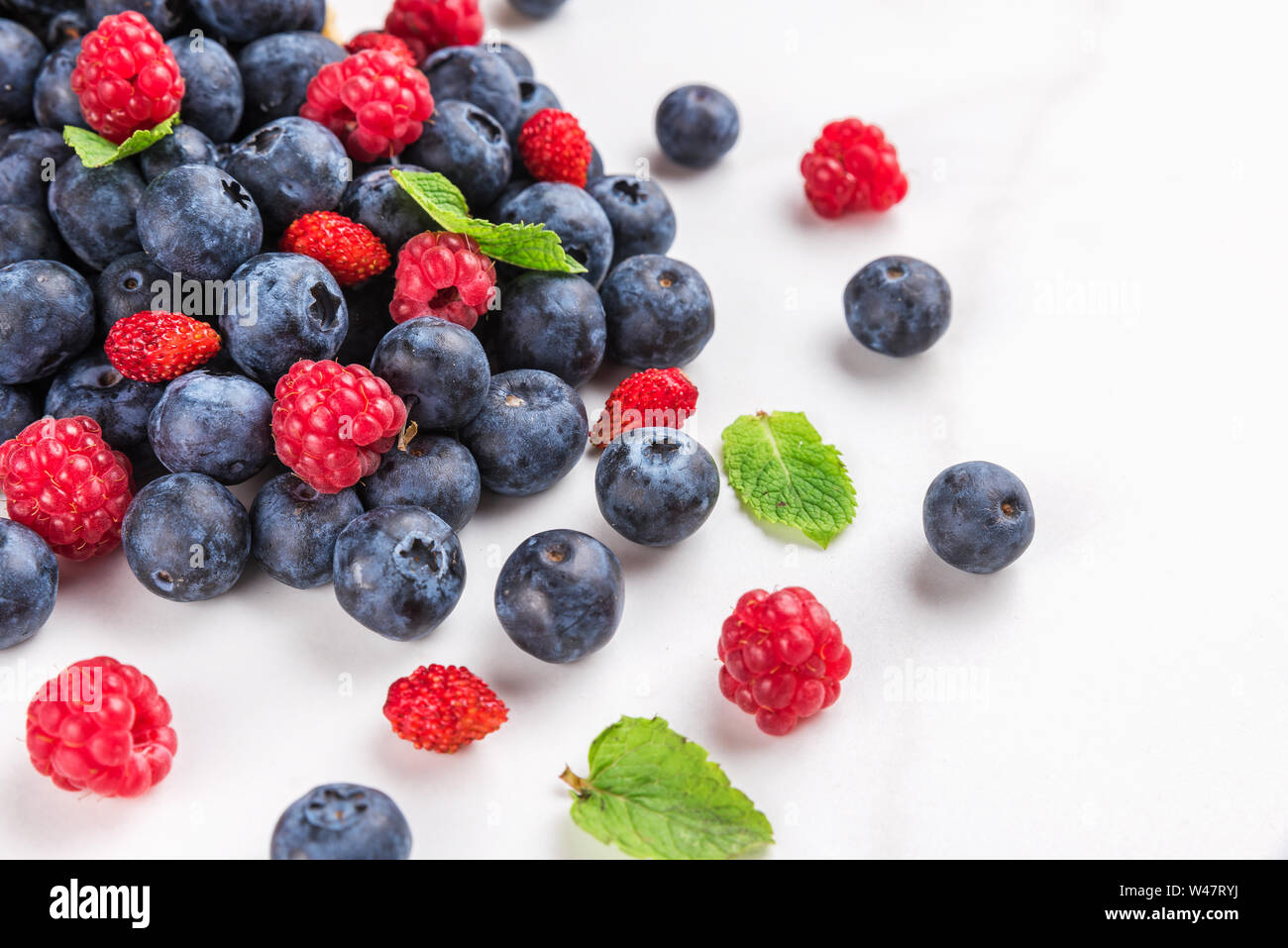 wild berries blueberry, strawberry and raspberry with mint on white marble background. summer food concept. close up Stock Photo