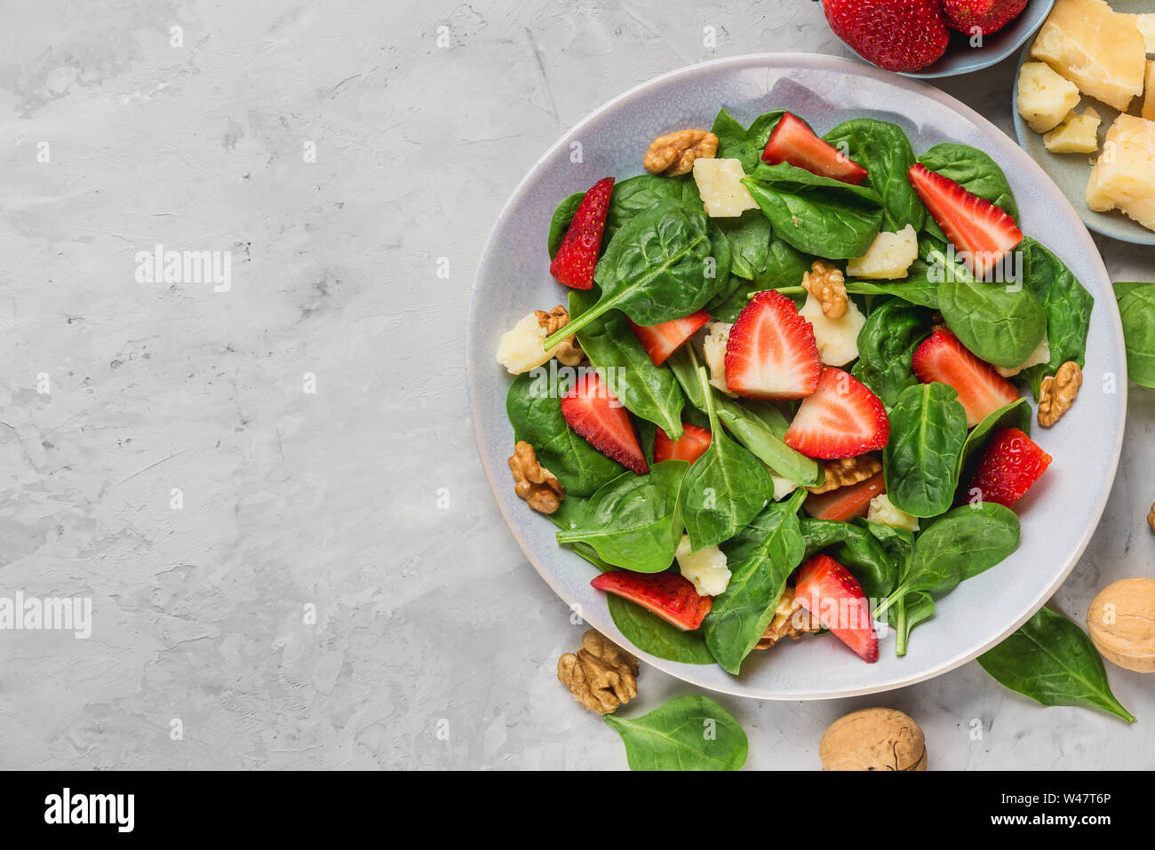 bowl of summer spinach salad with strawberry, parmesan cheese and walnuts on concrete background. healthy diet food. top view with copy space Stock Photo