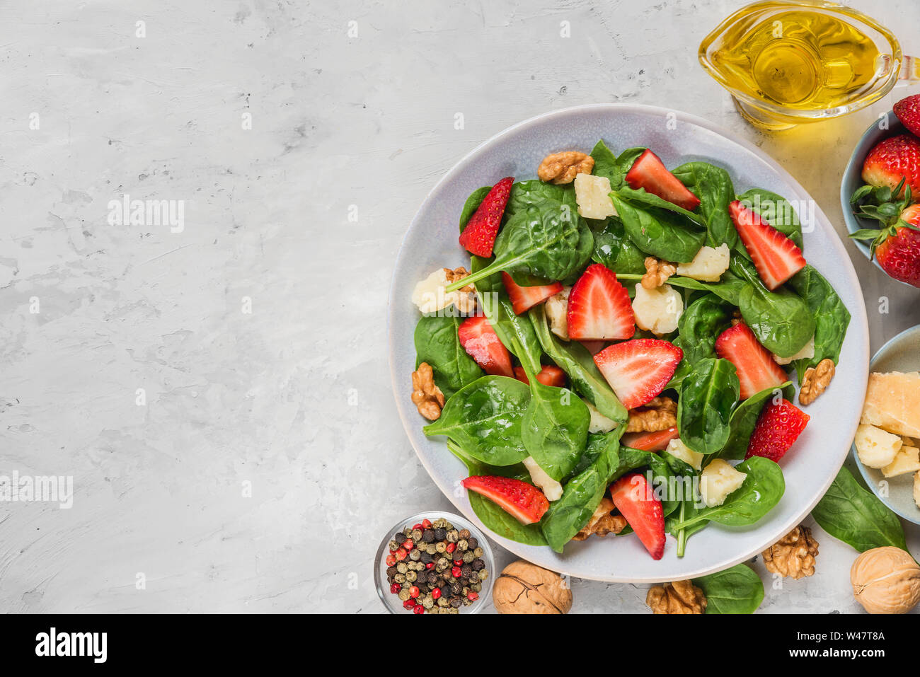 salad with strawberry, spinach leaves, parmesan cheese, olive oil and walnuts on concrete background. healthy diet food. top view with copy space Stock Photo