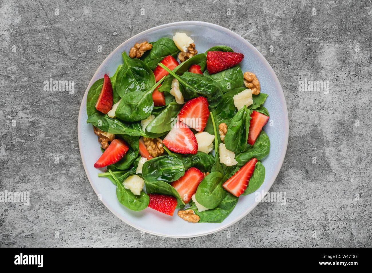salad with strawberry, spinach leaves, parmesan cheese and walnuts on concrete background. healthy diet food. top view Stock Photo