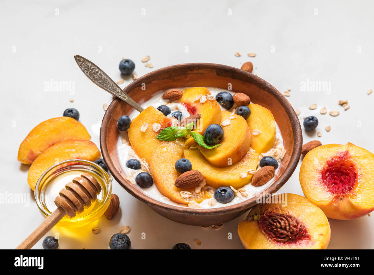 bowl of greek yogurt with peach, oats, nuts, mint, honey and blueberries with a spoon for healthy breakfast. close up Stock Photo