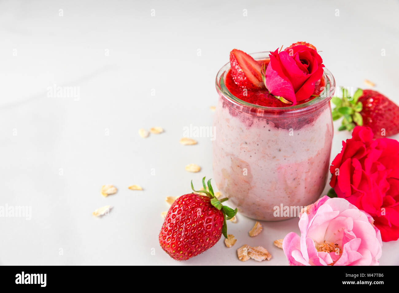 romantic healthy breakfast. overnight strawberry oats with fresh berries and mint with rose flowers in a glass on white marble table. close up Stock Photo