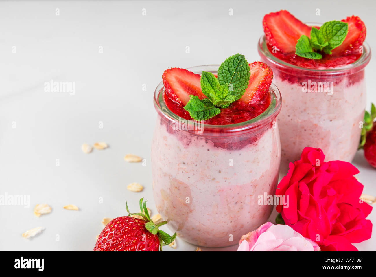 healthy diet breakfast dessert. strawberry overnight oats with fresh berries and mint with rose flowers on white marble table. close up Stock Photo