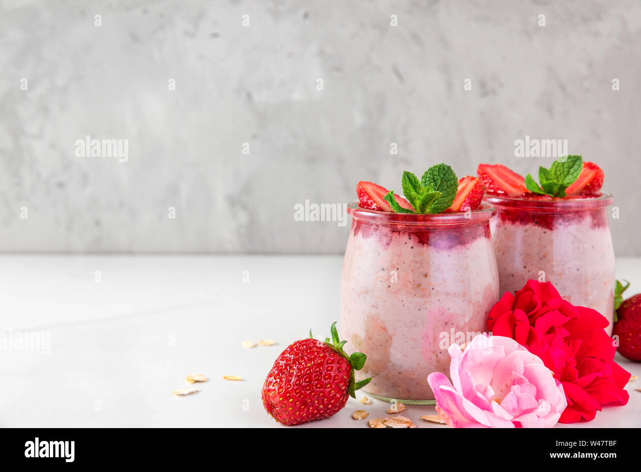 overnight oats or oatmeal porridge with fresh strawberries and mint in glasses with rose flowers on white marble table. healthy breakfast. close up Stock Photo