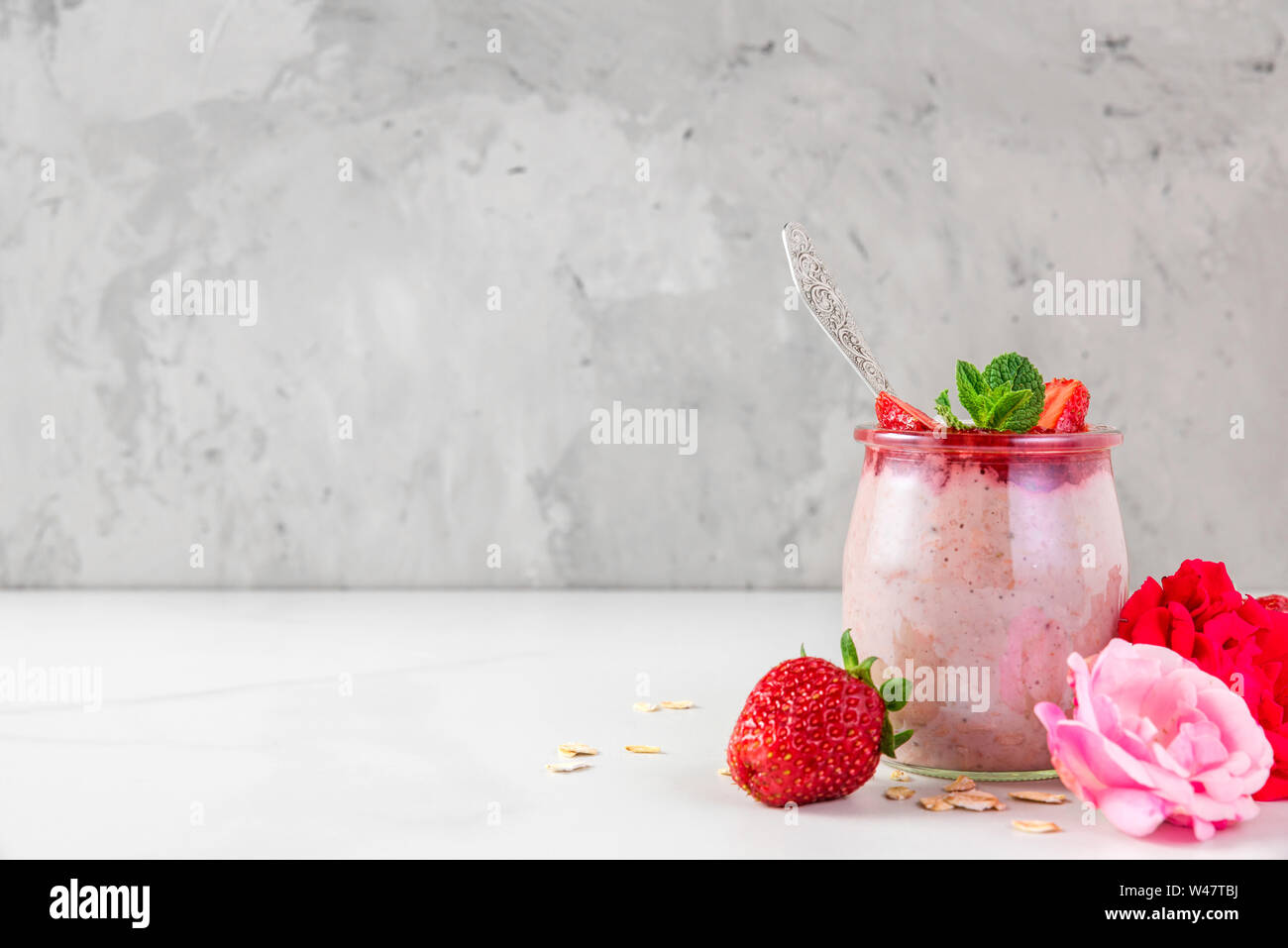 glass of strawberry oats with fresh berries, mint and rose flowers for healthy diet breakfast on white marble table. close up Stock Photo