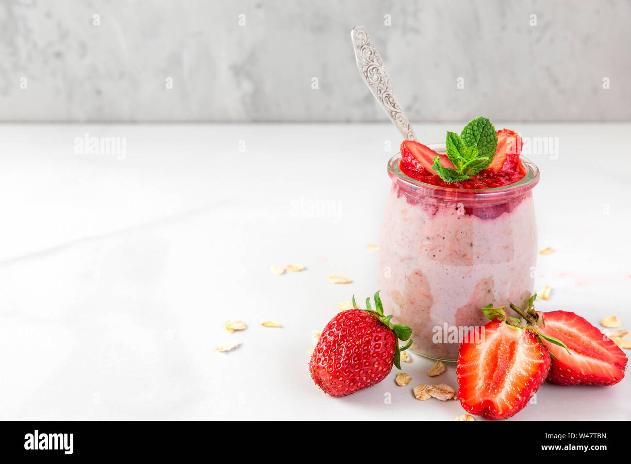 overnight oats with fresh strawberries and mint in a glass on white marble table. healthy diet breakfast. close up Stock Photo