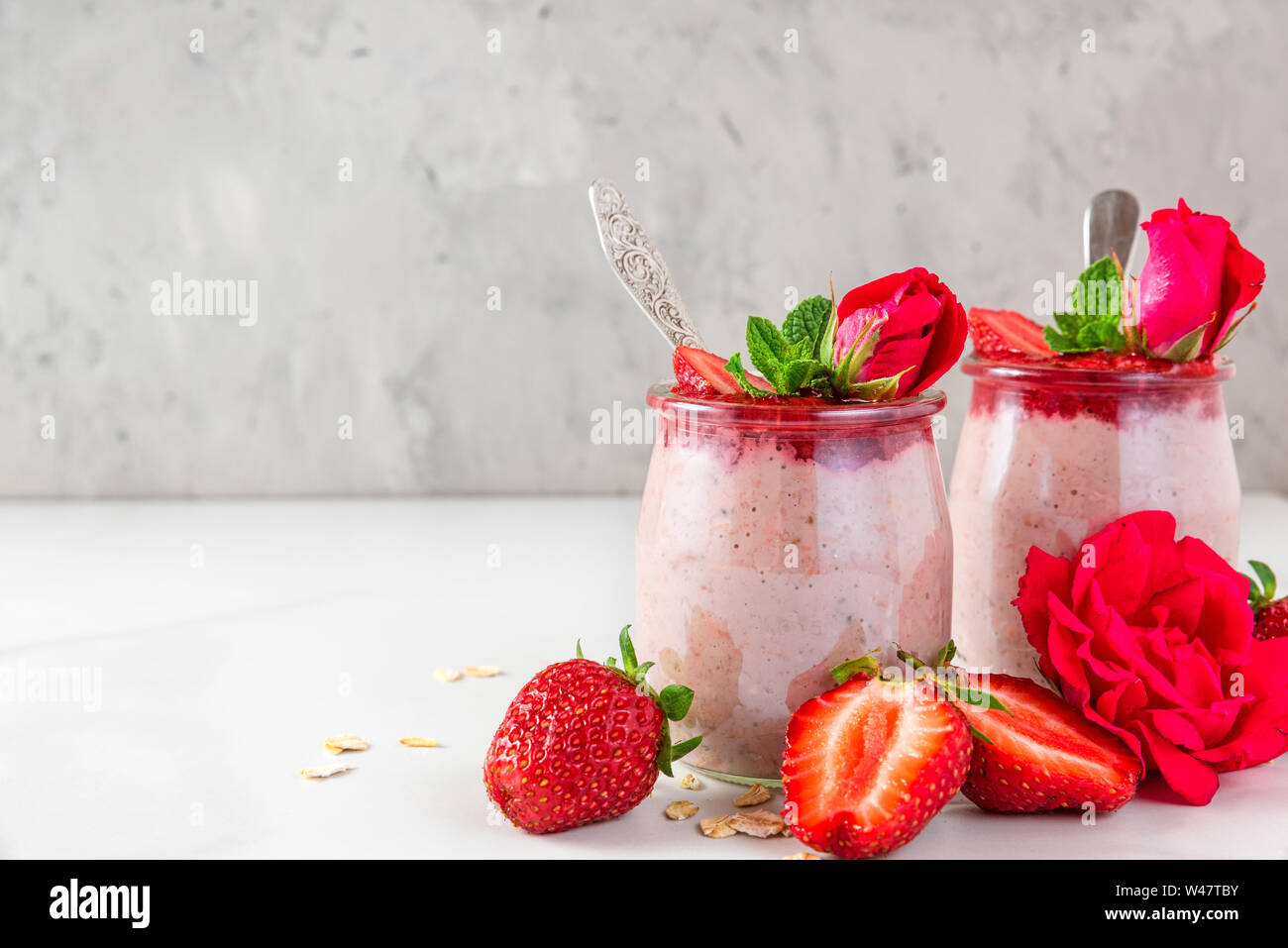 healthy diet breakfast dessert. strawberry overnight oats with fresh berries and mint with rose flowers on white marble table. close up Stock Photo