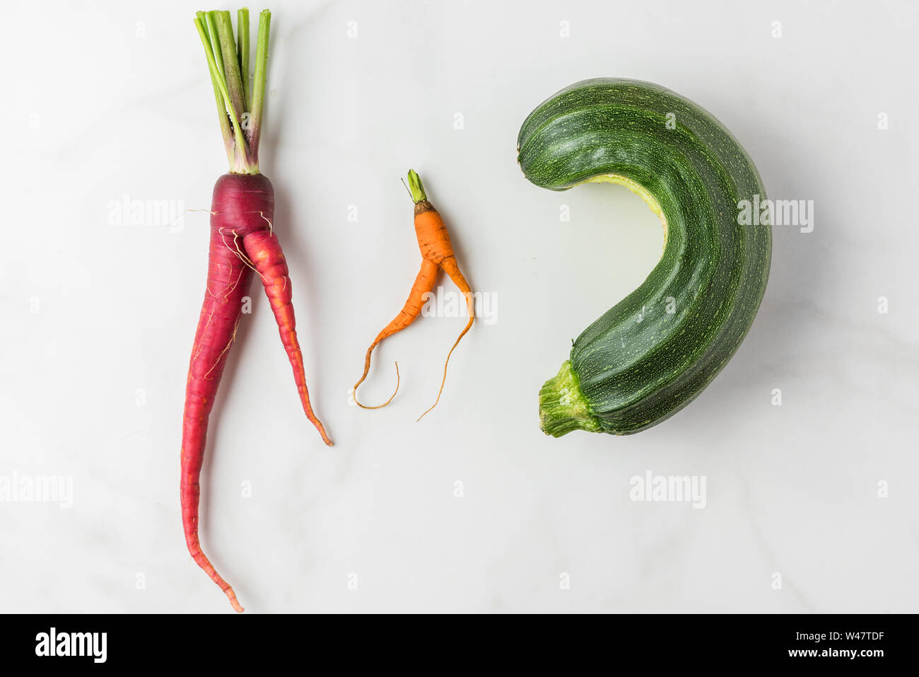 Trendy ugly organic carrots and zucchini from home garden on white marble table. top view. flat lay Stock Photo
