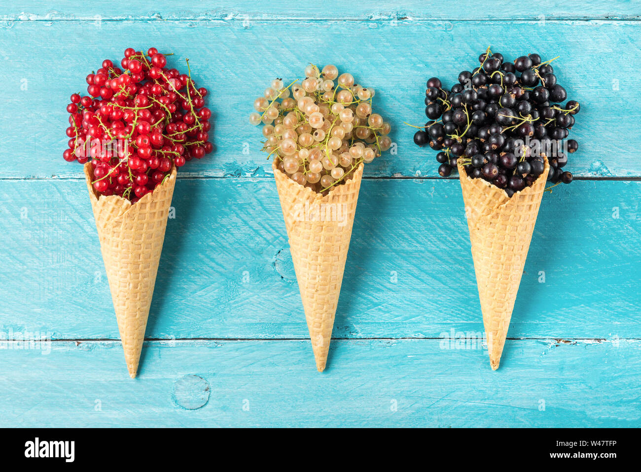 assortment of currant berries black, red and white in waffle ice cream cone on blue wooden background. creative summer food concept. flat lay. top vie Stock Photo