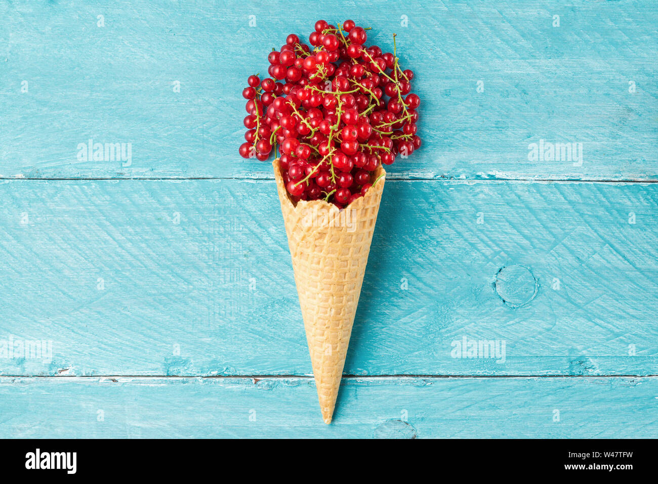 red currant berries in waffle ice cream cone on blue wooden background. creative summer food concept. flat lay. top view Stock Photo