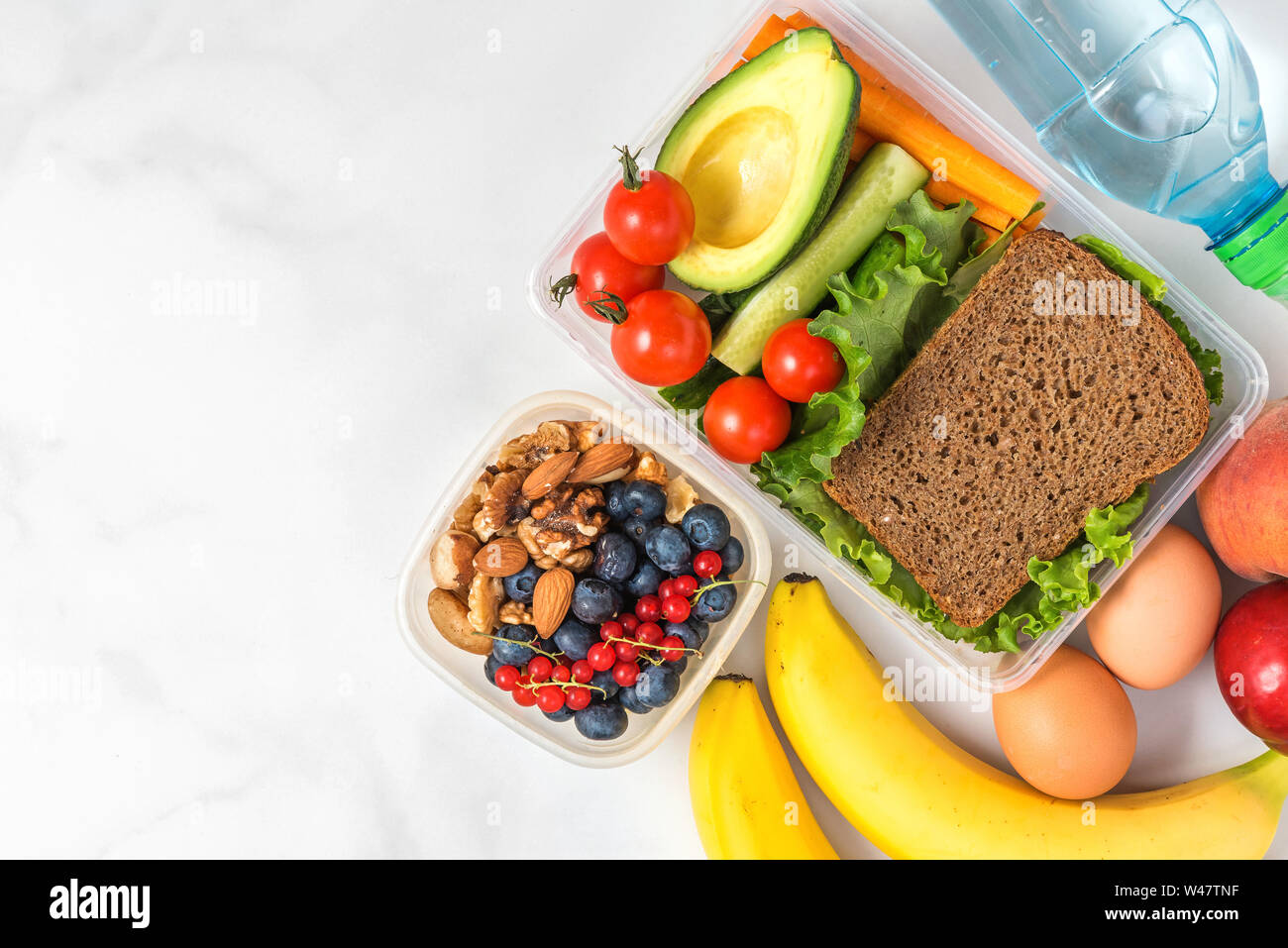 Lunch boxes with food ready to go for work or school. sandwich, vegetables, avocado, nuts, berries, eggs and water. meal preparation or dieting concep Stock Photo