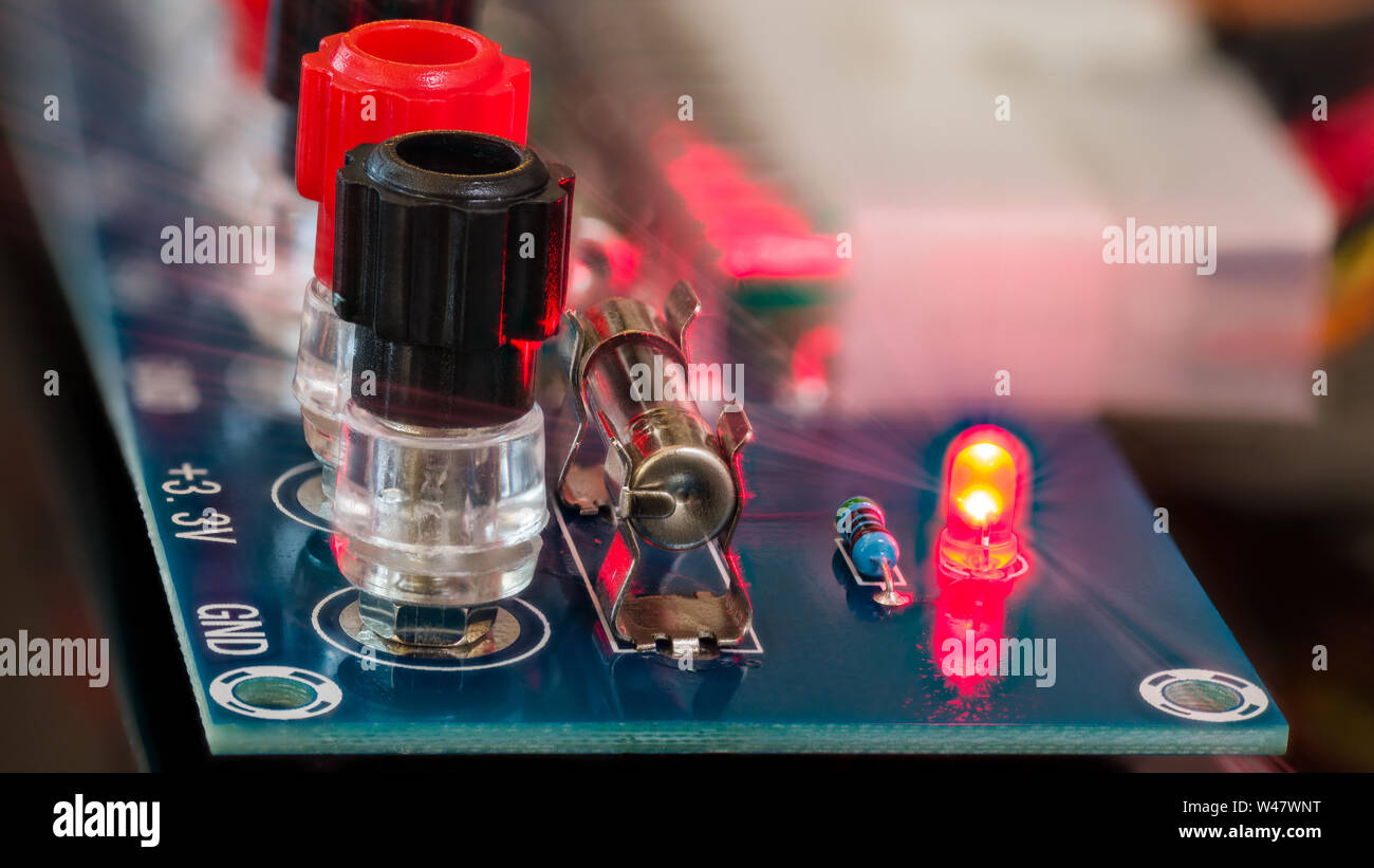 Power supply unit diagnostics. Electronic components detail on blue circuit board. Screw terminals, miniature fuse, red LED diode, resistor. Light ray. Stock Photo
