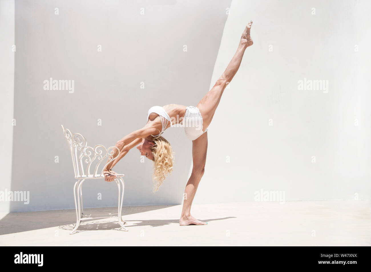 Classical beauty in yoga wheel pose or upward bow posture utilizing a beautiful chair as a prop. This woman is a ballerina turned yogi. Stock Photo