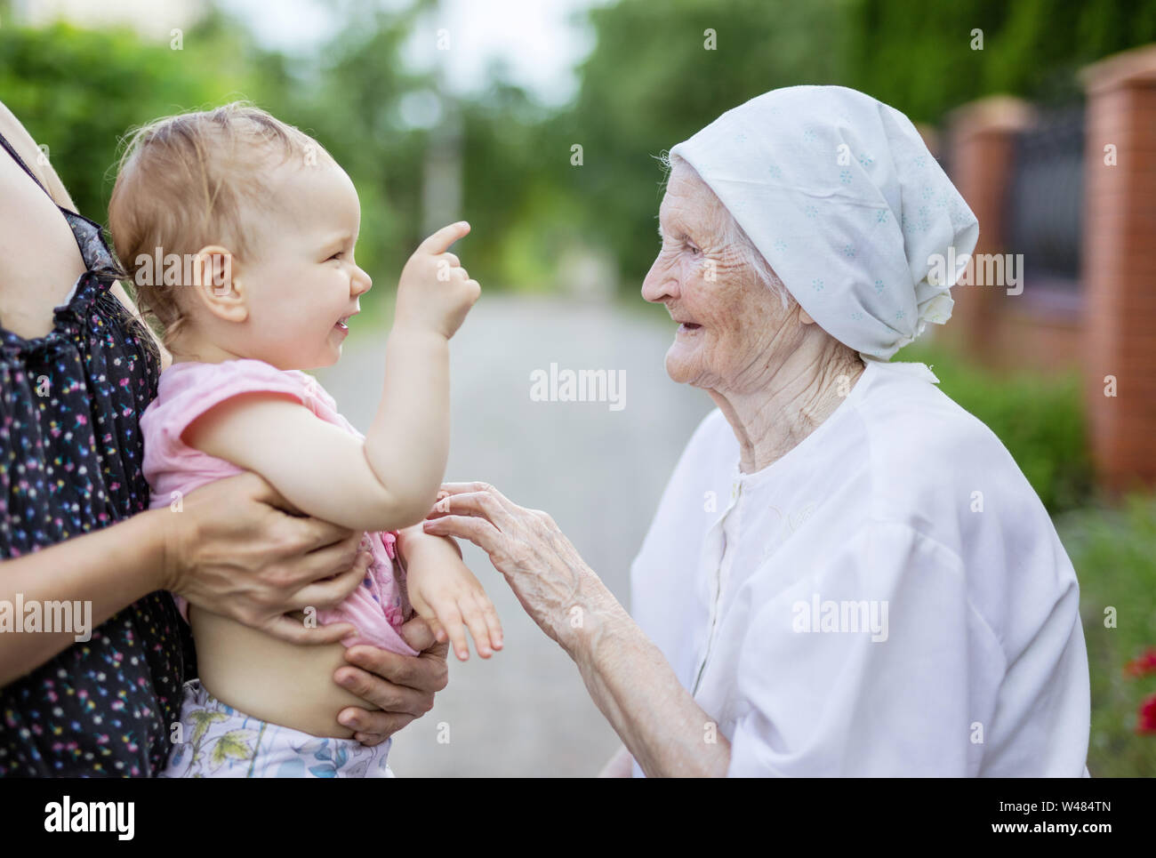 Cute toddler girl playing with her great grandmother and laughing. Cropped view of mother holding little daughter. Stock Photo