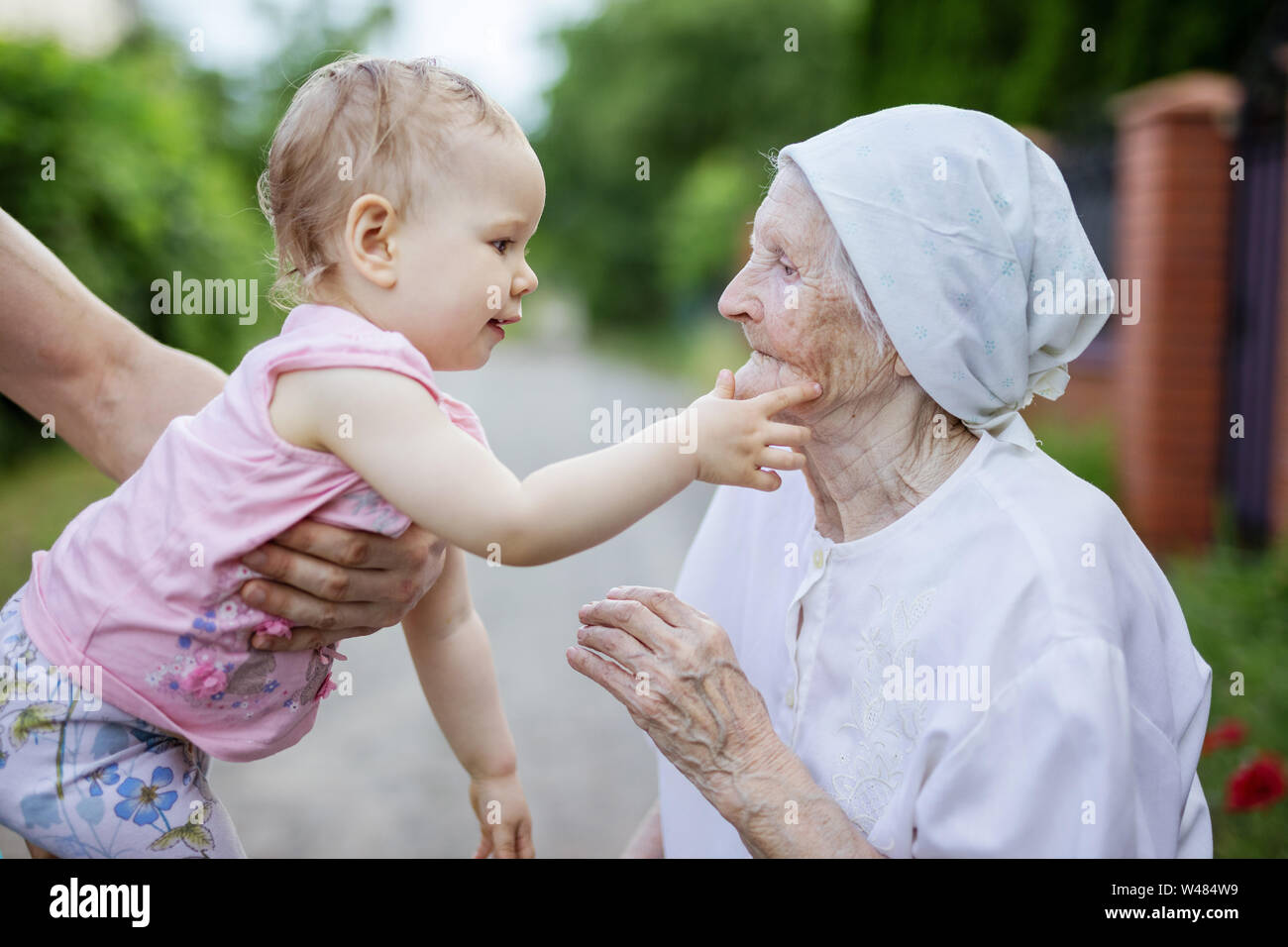 Cute toddler girl playing with her great grandmother and touching her face outdoors Stock Photo