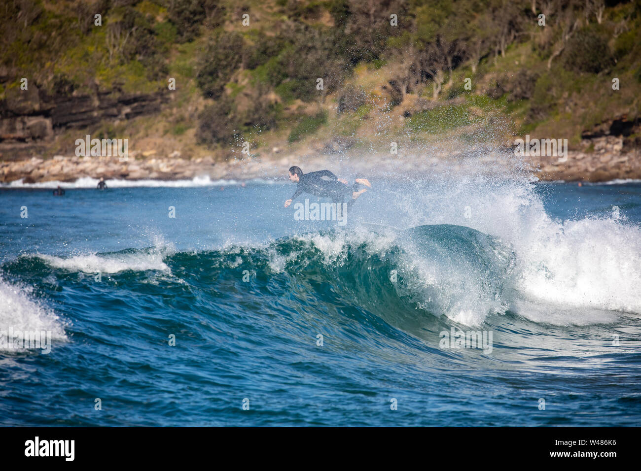 Male surfer in wetsuit jumps over wave at Avalon beach in Sydney