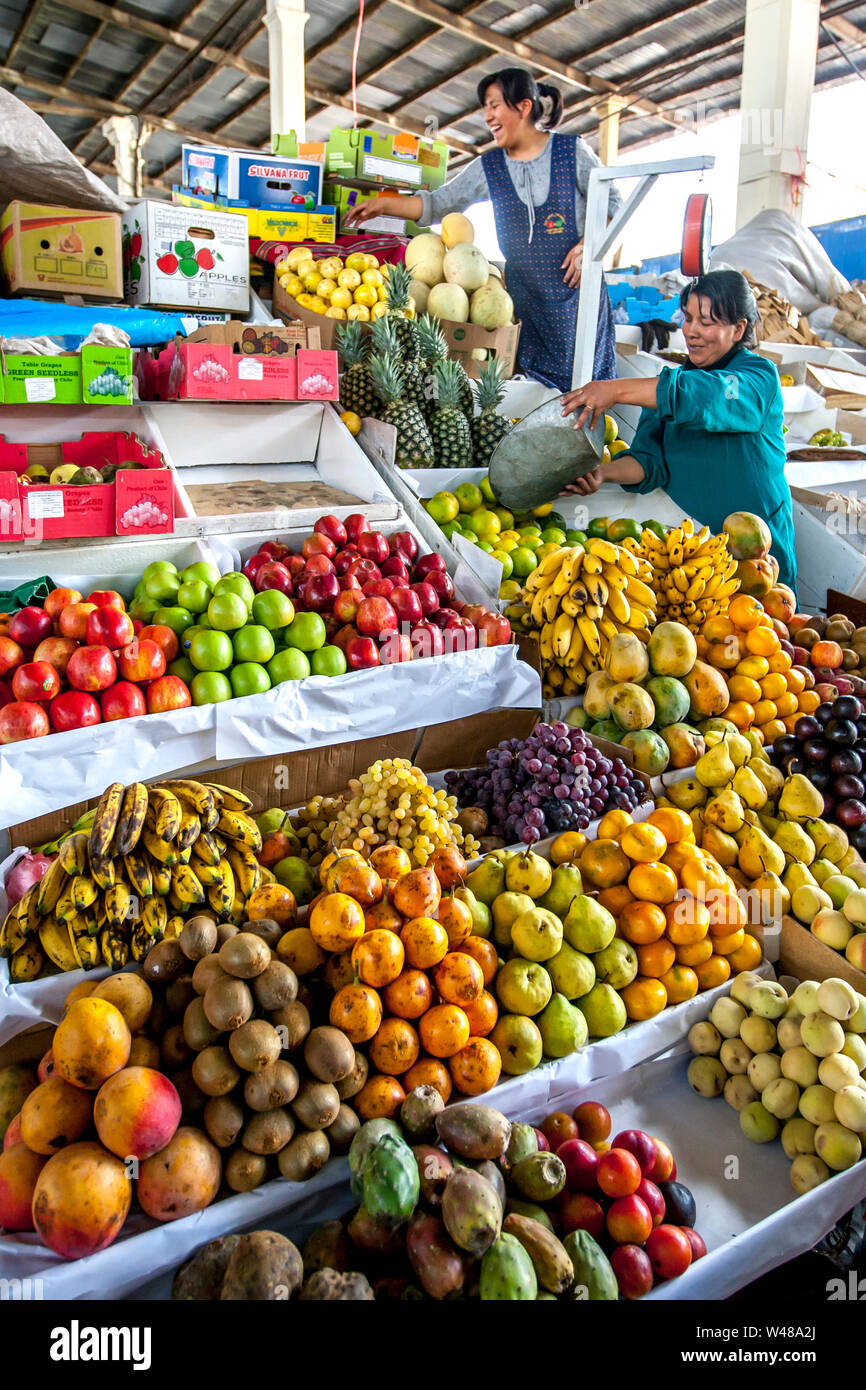 Ladies stack a variety of colourful fresh fruit and vegetables at their stall in the undercover market in central Cusco in Peru. Stock Photo
