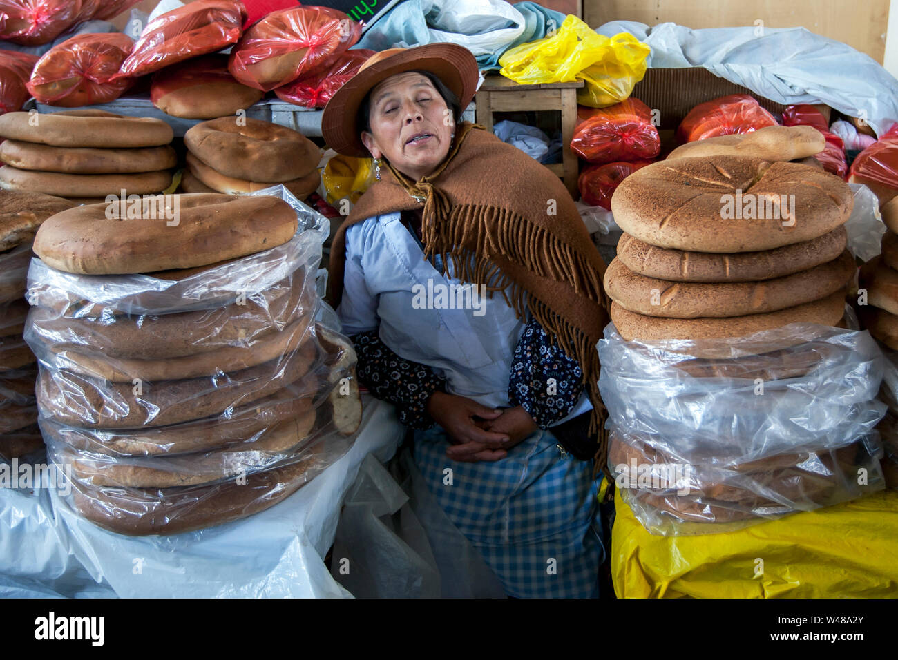 A shopkeeper sleeping between the fresh bread rolls at a stall within the undercover market at Cusco in Peru. Stock Photo