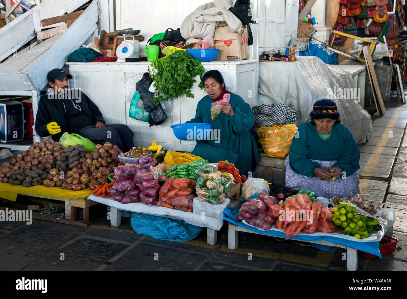 A family selling a variety of fresh fruit and vegetables sit at their stall inside the undercover market in central Cusco in Peru. Stock Photo