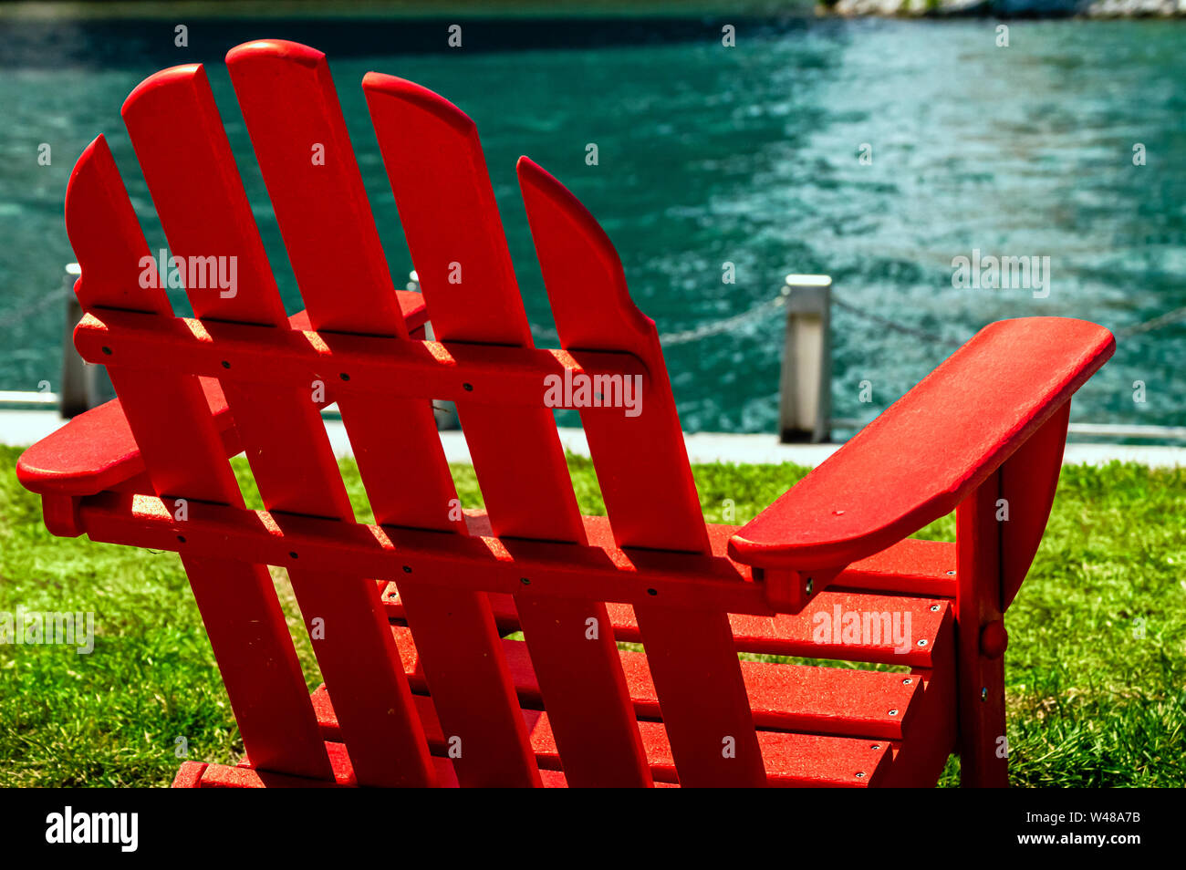 A red wooden lawn chair on the waterfront riverwalk on a sunny day