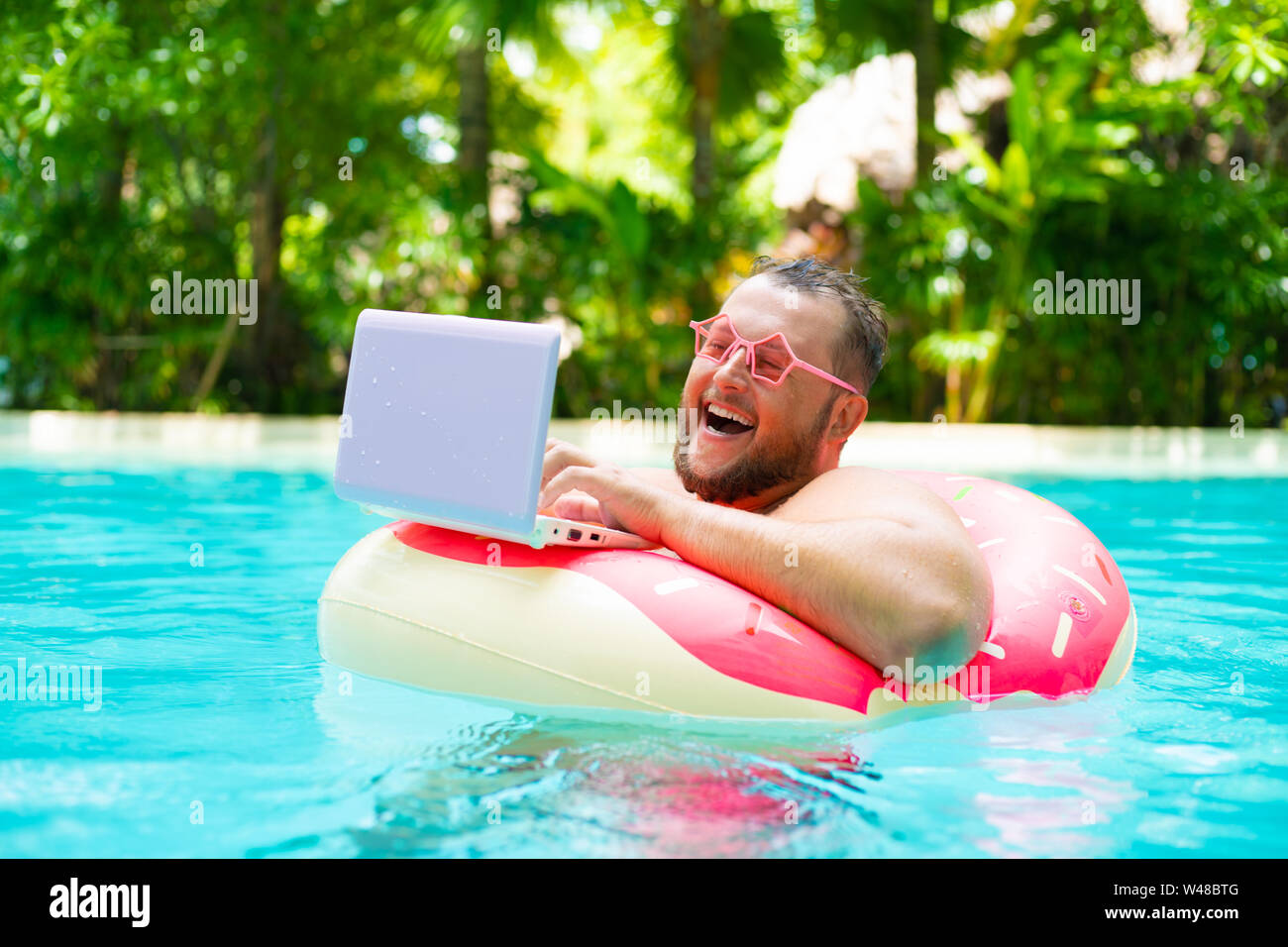 laughing Fat funny man in pink inflatable circle in pink glasses works on a  laptop in a swimming pool Stock Photo - Alamy