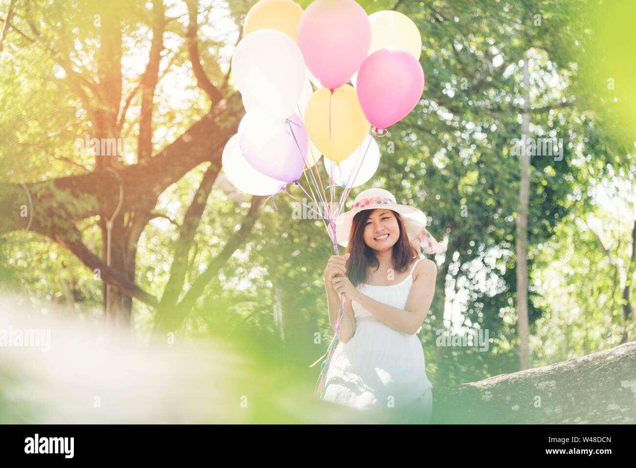 Beautiful young woman holding air balloons in garden Stock Photo