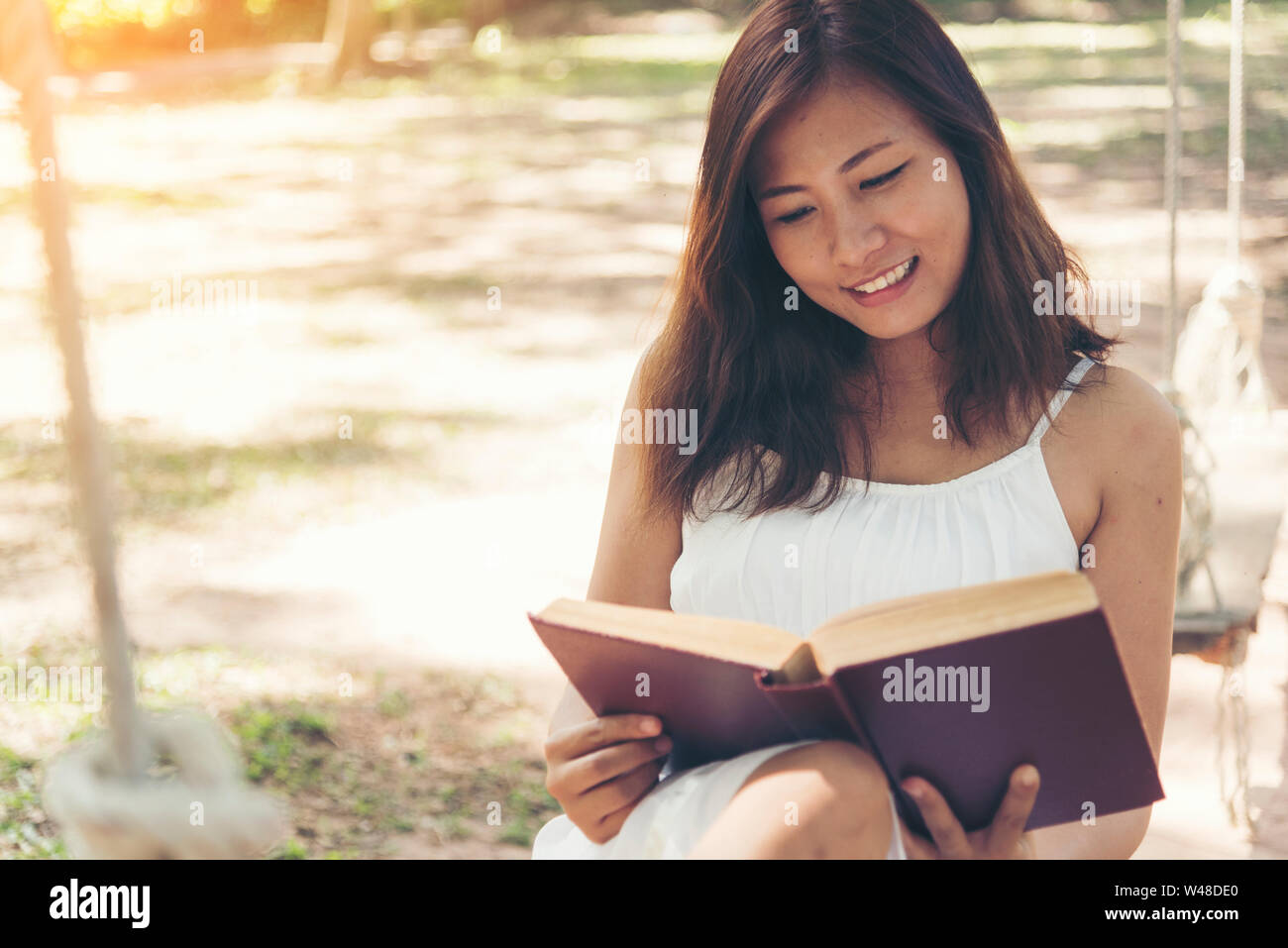 Young beautiful woman reading a book in the park with smiling face. Stock Photo