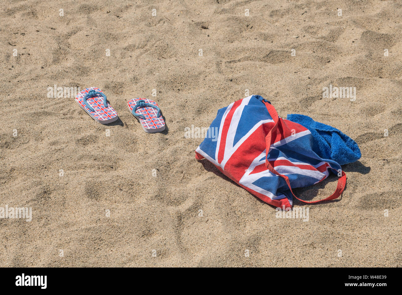 Union Jack beach bag & flip-flops on sandy beach - for 2021 UK staycation, holidays at home, staycation Cornwall, seaside holiday, flip-flop footwear. Stock Photo