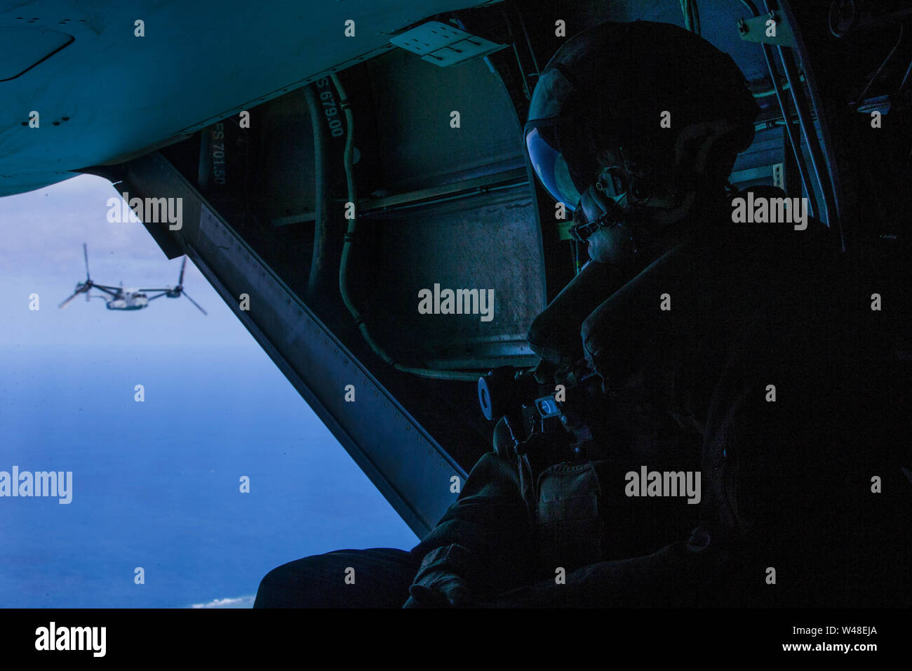 A Marine with Marine Medium Tiltrotor Squadron 265 (Reinforced), 31st Marine Expeditionary Unit, peers out of the back of an MV-22B Osprey tiltrotor aircraft after departing the amphibious assault ship USS Wasp (LHD 1), July 19, 2019. Wasp, flagship of the Wasp Amphibious Ready Group, with embarked 31st MEU, is currently participating in Talisman Sabre 2019 off the coast of Northern Australia. A bilateral, biennial event, Talisman Sabre is designed to improve U.S. and Australian combat training, readiness and interoperability through realistic, relevant training necessary to maintain regional Stock Photo