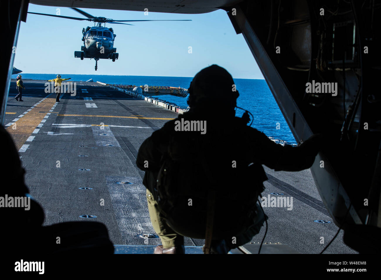 A Marine with Marine Medium Tiltrotor Squadron 265 (Reinforced), 31st Marine Expeditionary Unit, observes an MH-60S Sea Hawk with Helicopter Sea Combat Squadron 25 out of the back of an MV-22B Osprey tiltrotor aircraft aboard the amphibious assault ship USS Wasp (LHD 1), July 19, 2019. Wasp, flagship of the Wasp Amphibious Ready Group, with embarked 31st MEU, is currently participating in Talisman Sabre 2019 off the coast of Northern Australia. A bilateral, biennial event, Talisman Sabre is designed to improve U.S. and Australian combat training, readiness and interoperability through realisti Stock Photo