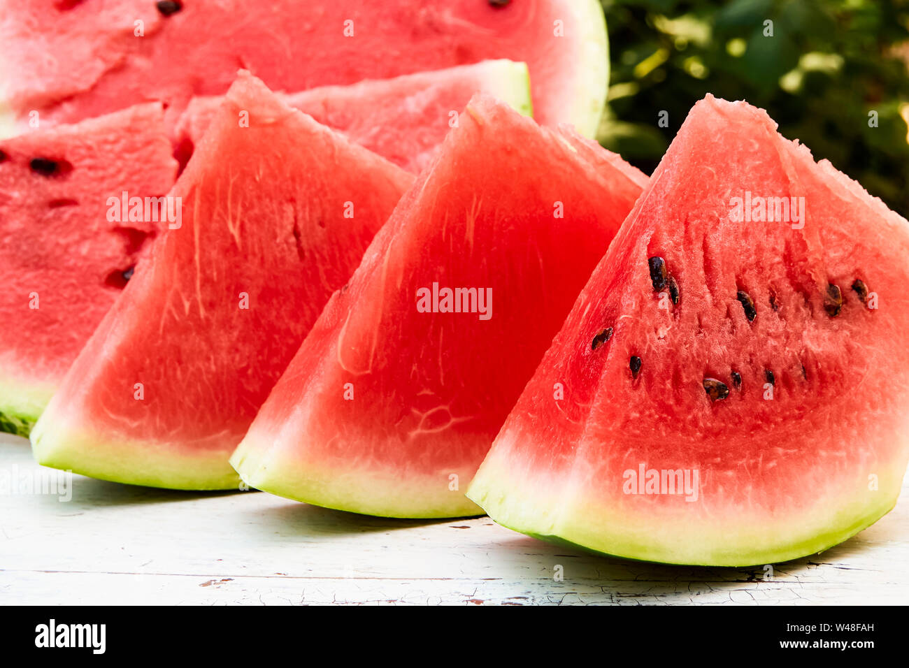 Fresh ripe striped sliced watermelon on a wooden old table, against the background of green leaves, outdoors. Stock Photo