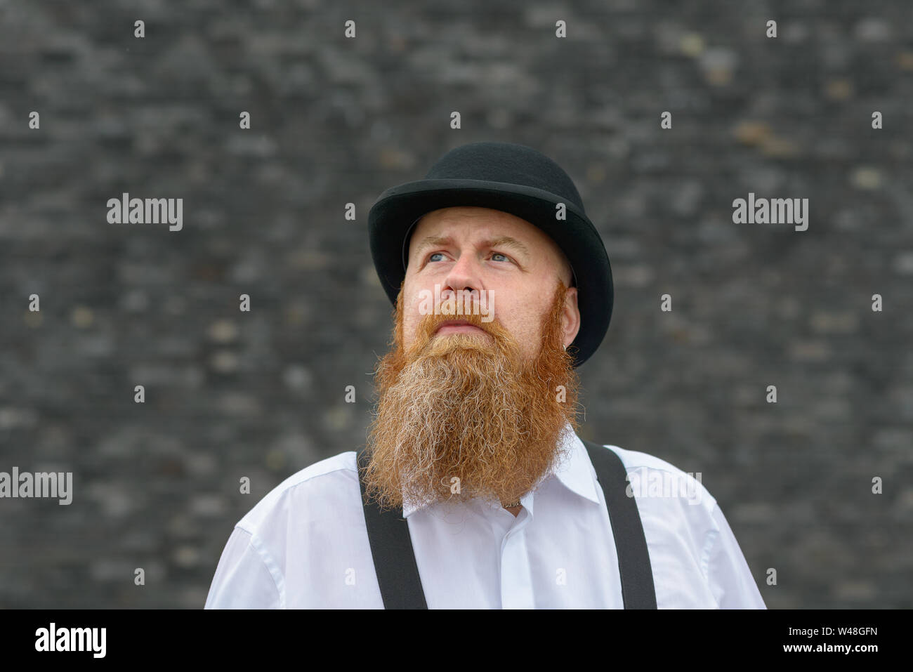 Thoughtful man with bushy red beard in bowler hat looking to blank copy ...